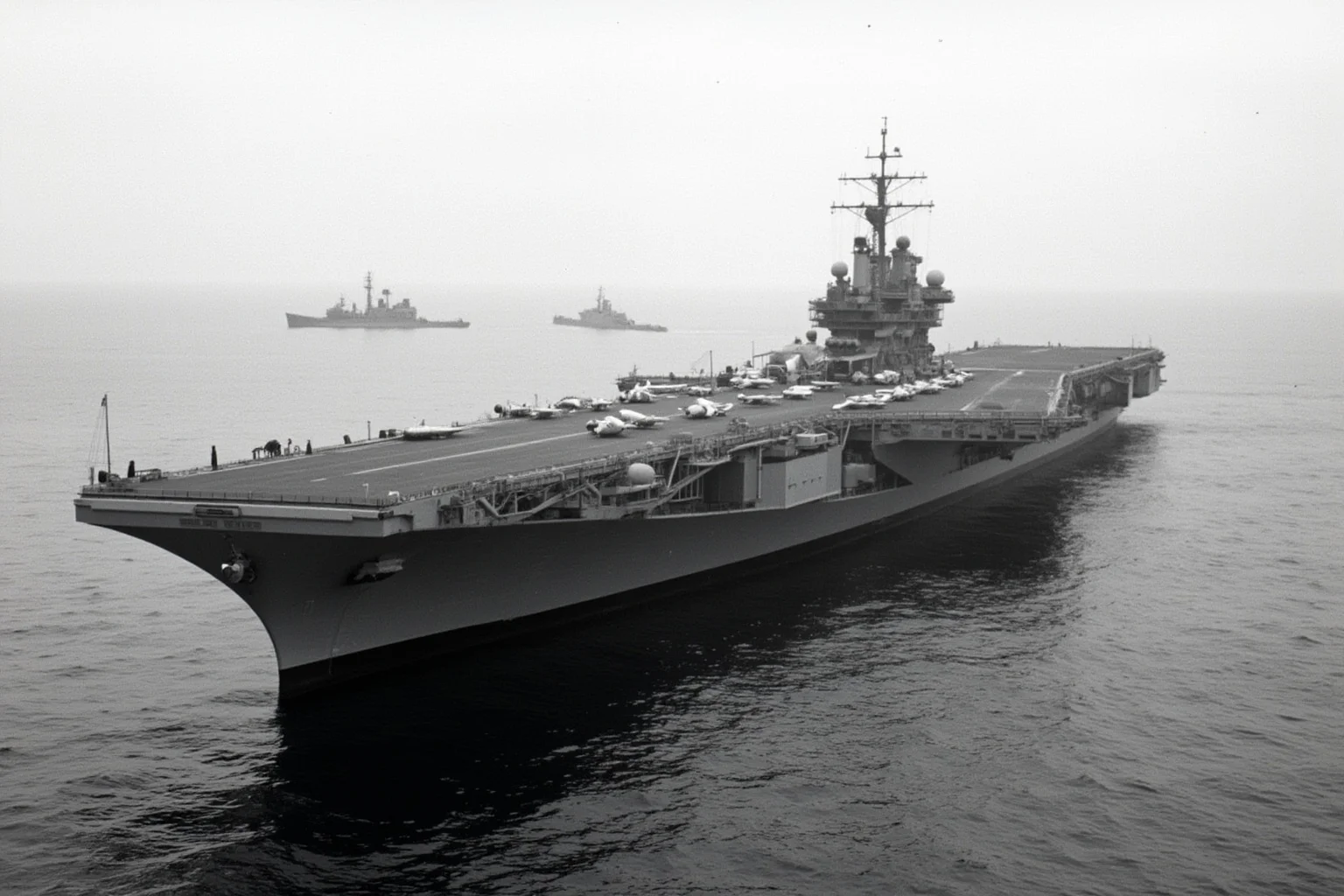The Longest-Serving Warships of All Time 18 1960s nuclear-powered aircraft carrier with flat deck and multiple radar masts, at sea with escort ships in the distance
