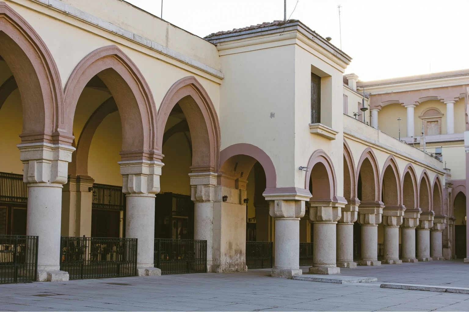 Exterior view of a Renaissance-era hospital facade with a covered arcade, rounded arches, and slender columns in soft morning light