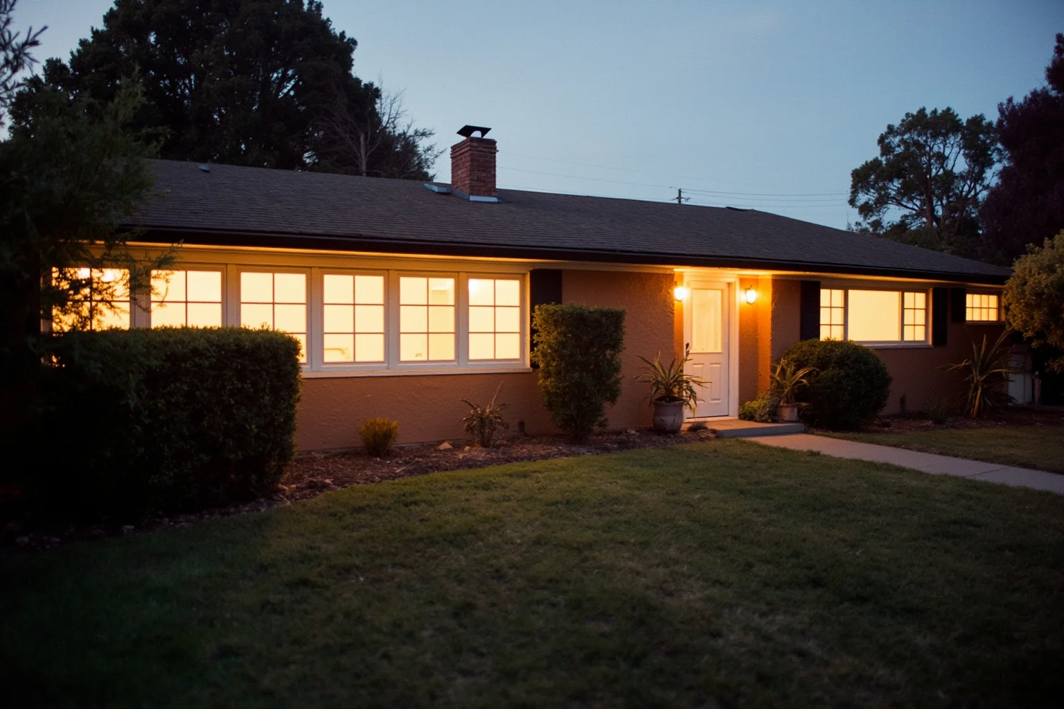 A 1960s California ranch house exterior with warm evening light, hinting at cult-era unease