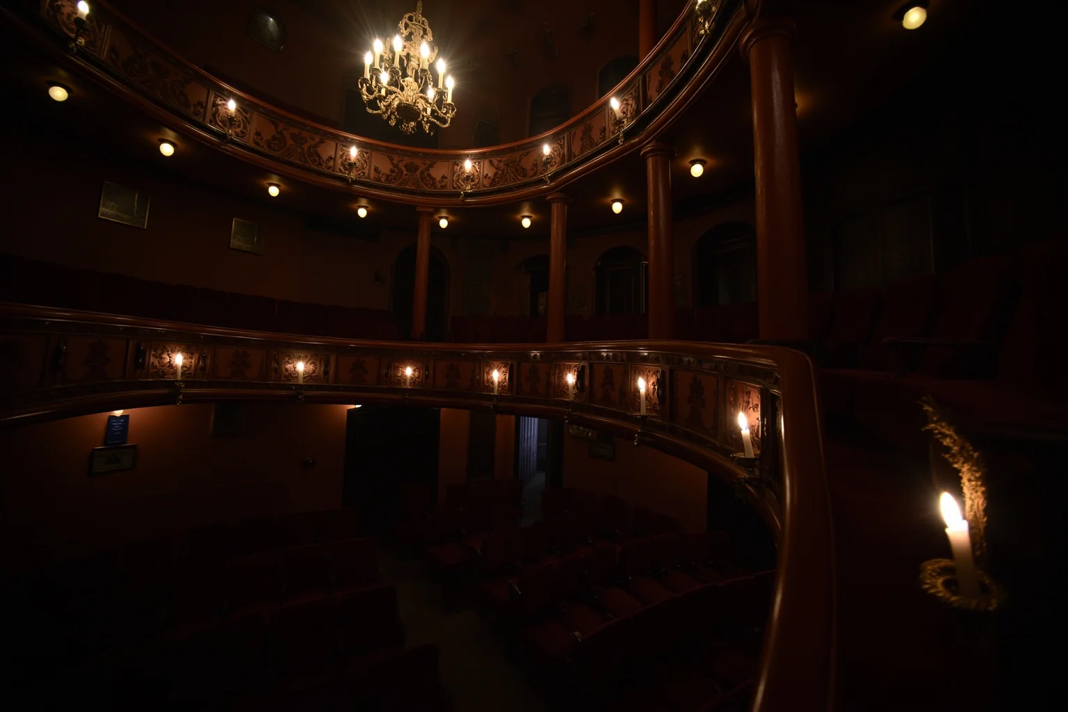 A 19th-century theater balcony interior with red velvet seats and dim gaslight