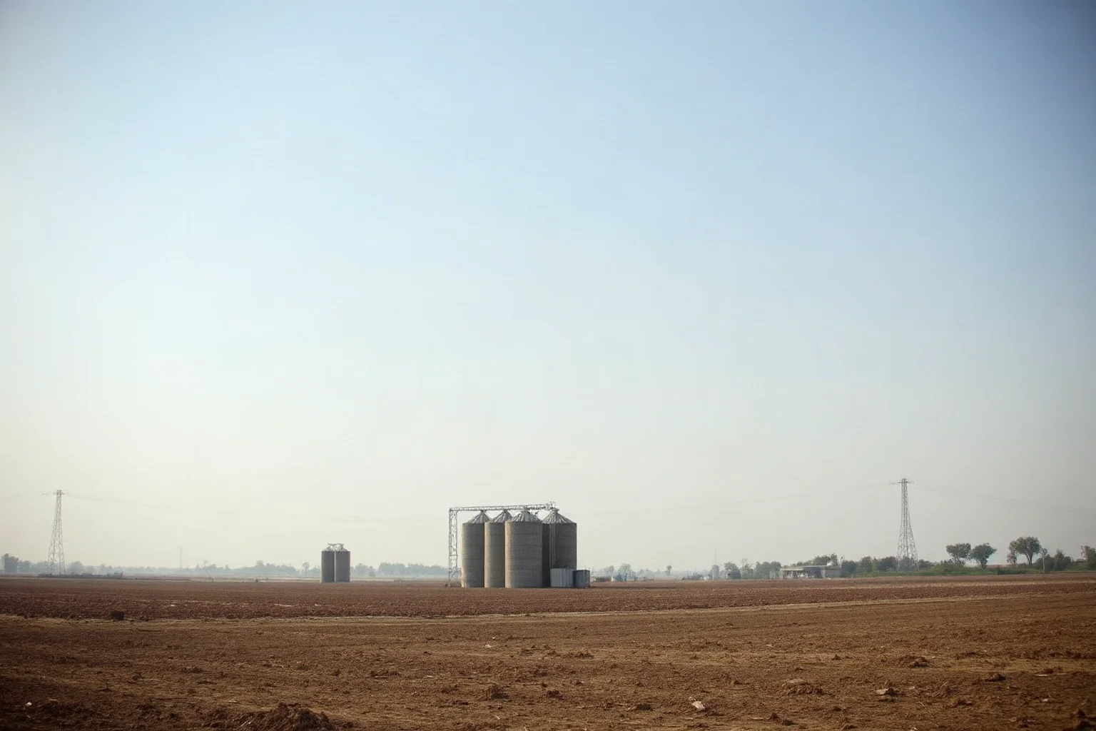 A barren failed farmland landscape with empty grain silos under a hazy sky, representing famine caused by policy failure