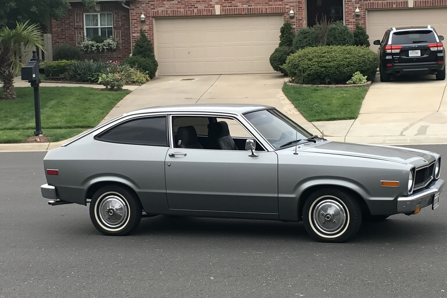 A boxy 1970s subcompact hatchback in a muted color parked in a suburban driveway