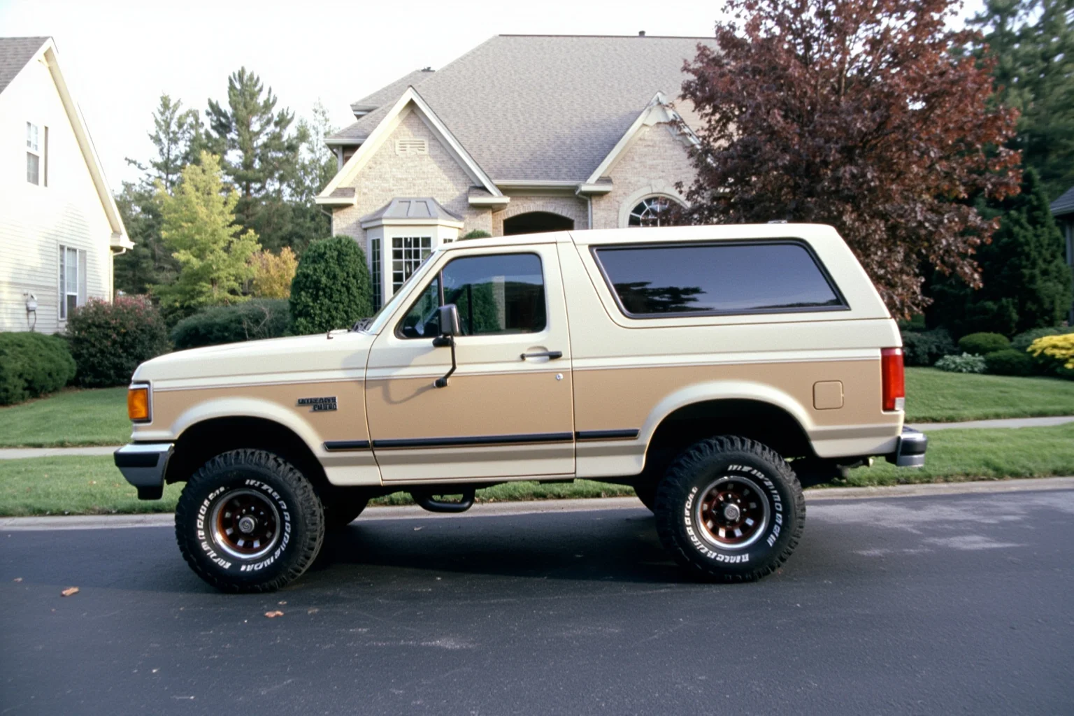 A boxy early-1990s midsize SUV with a two-tone paint job parked in front of a suburban home