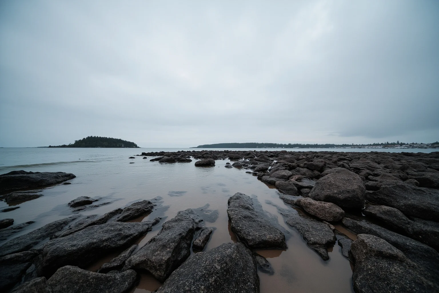 A calm empty rocky shoreline with no footprints, eerie stillness, overcast sky