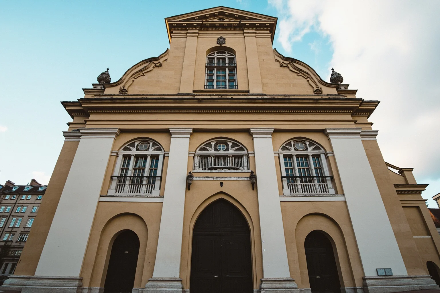 A church facade blending pointed Gothic doorways below with a classical pedimented upper section and scroll volutes