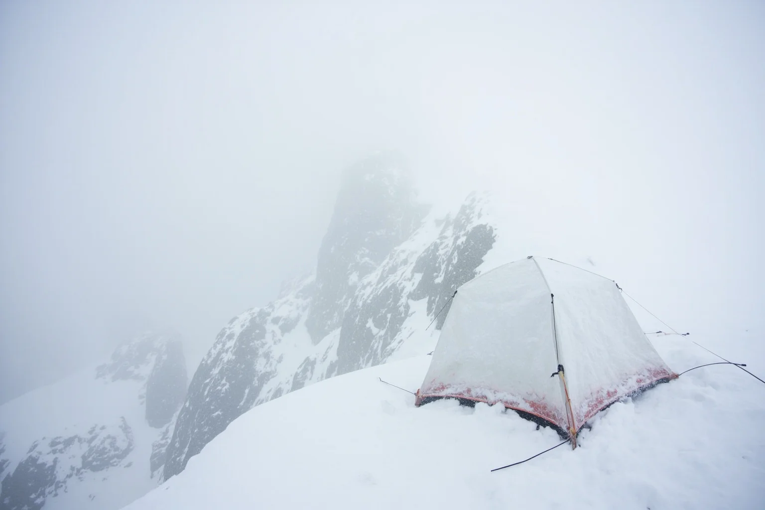 A climber's tent battered by whiteout blizzard conditions on a high snowy mountain ridge
