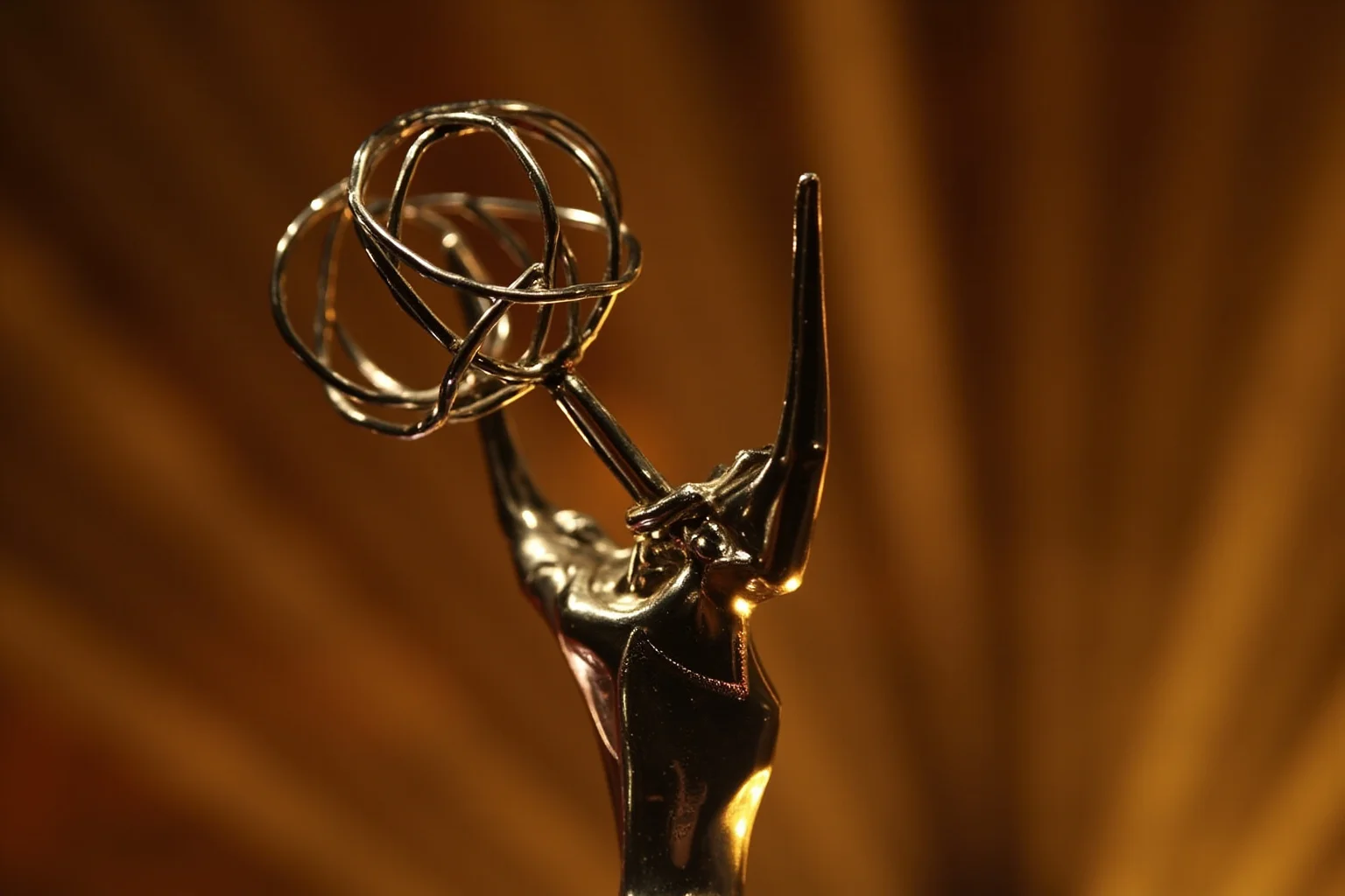 A close-up of an ornate Tony Award trophy on a stage backdrop with soft golden lighting