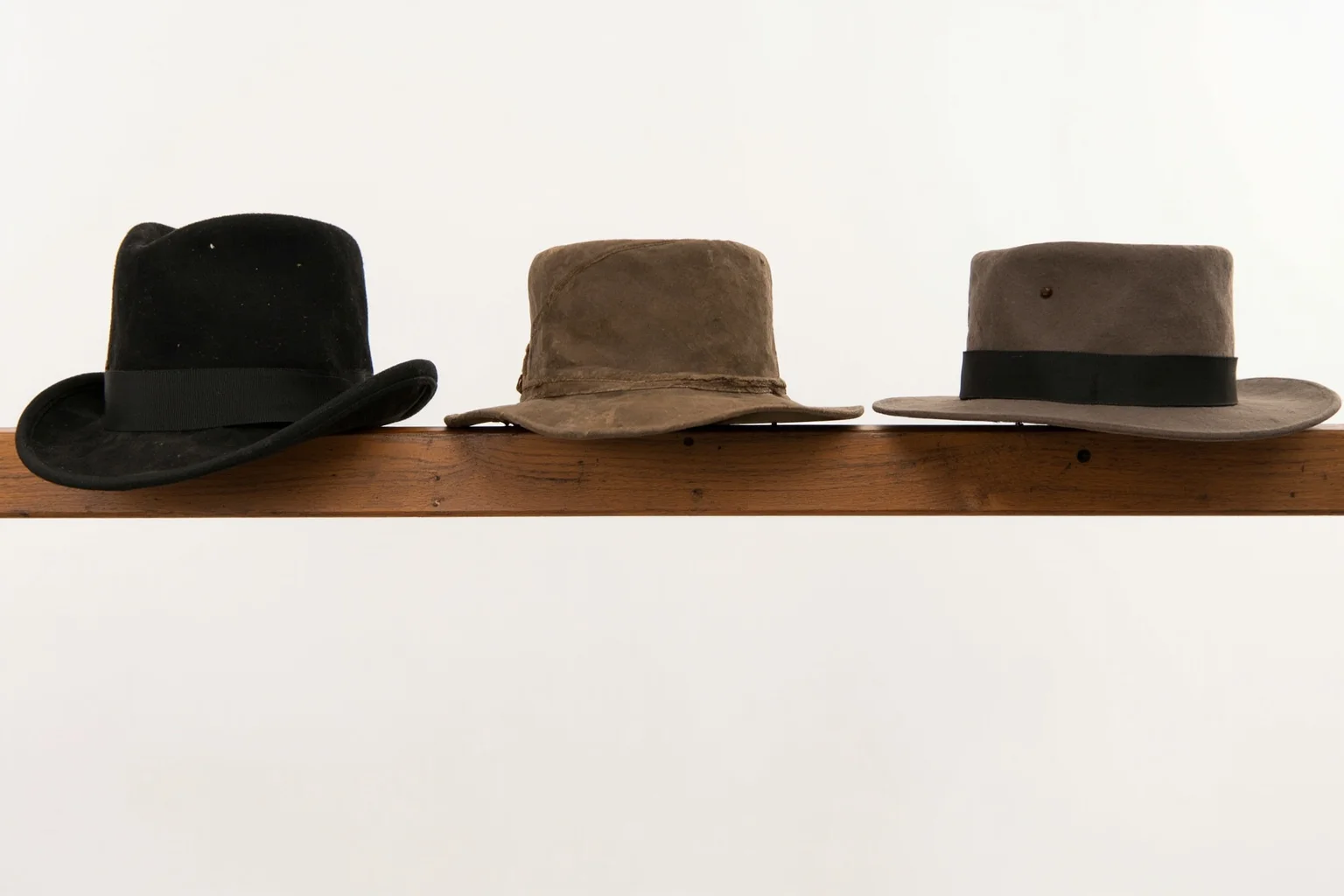 A collection of different 19th-century western hat styles including a bowler and a smaller-brimmed hat on a wooden rail