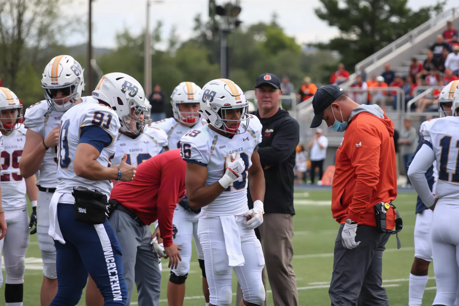A college football player being tended to by medical staff on the field during a kickoff return, teammates gathered nearby