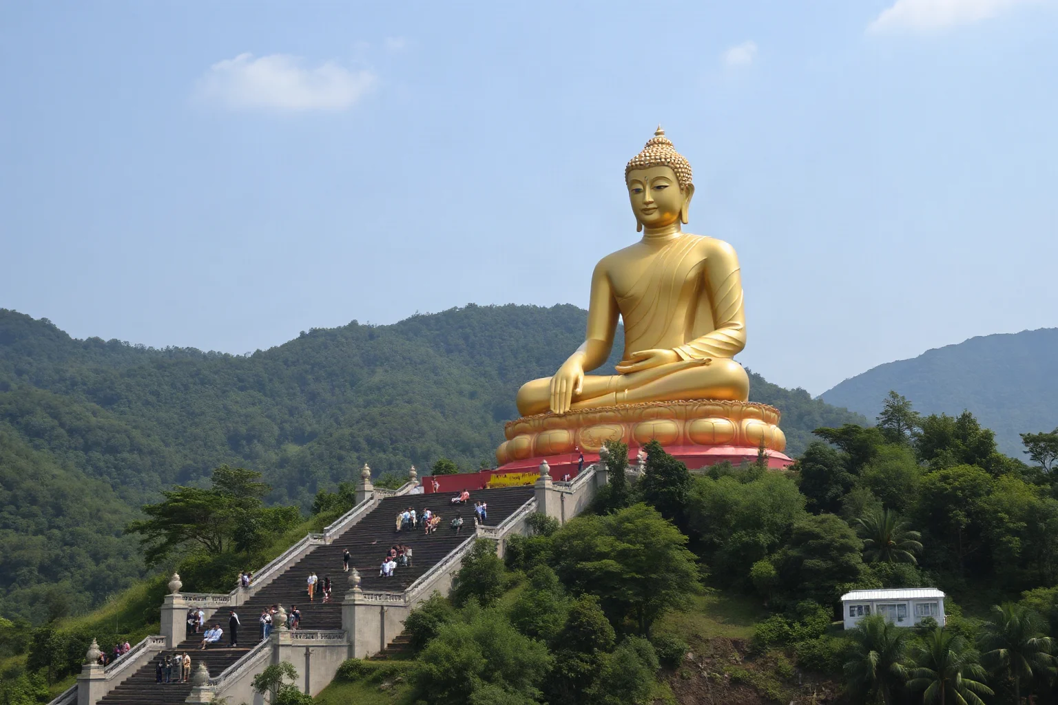 A colossal seated golden Buddha statue on a hillside surrounded by green mountains