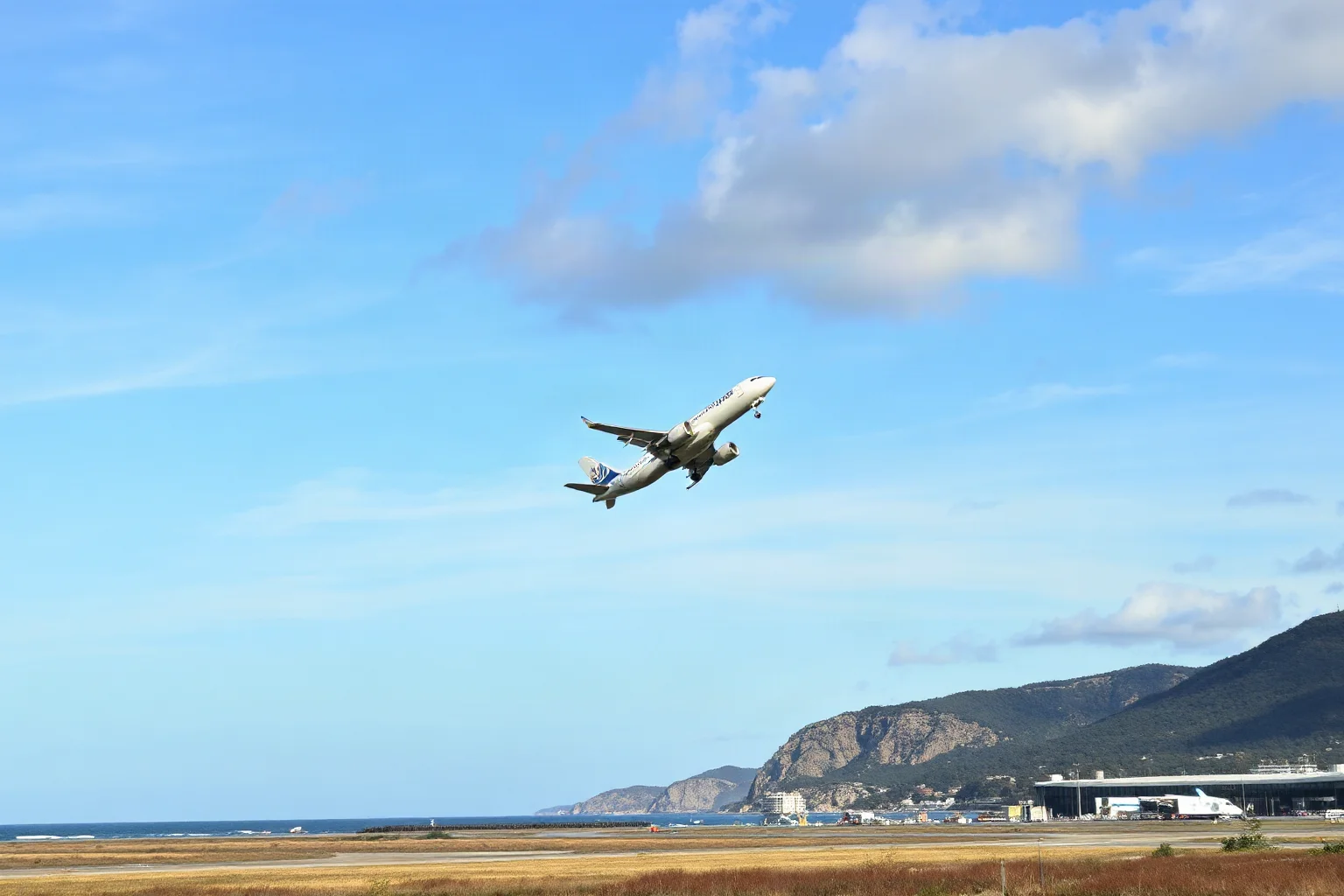 A commercial jet climbing steeply into a blue sky just after takeoff from a coastal airport runway