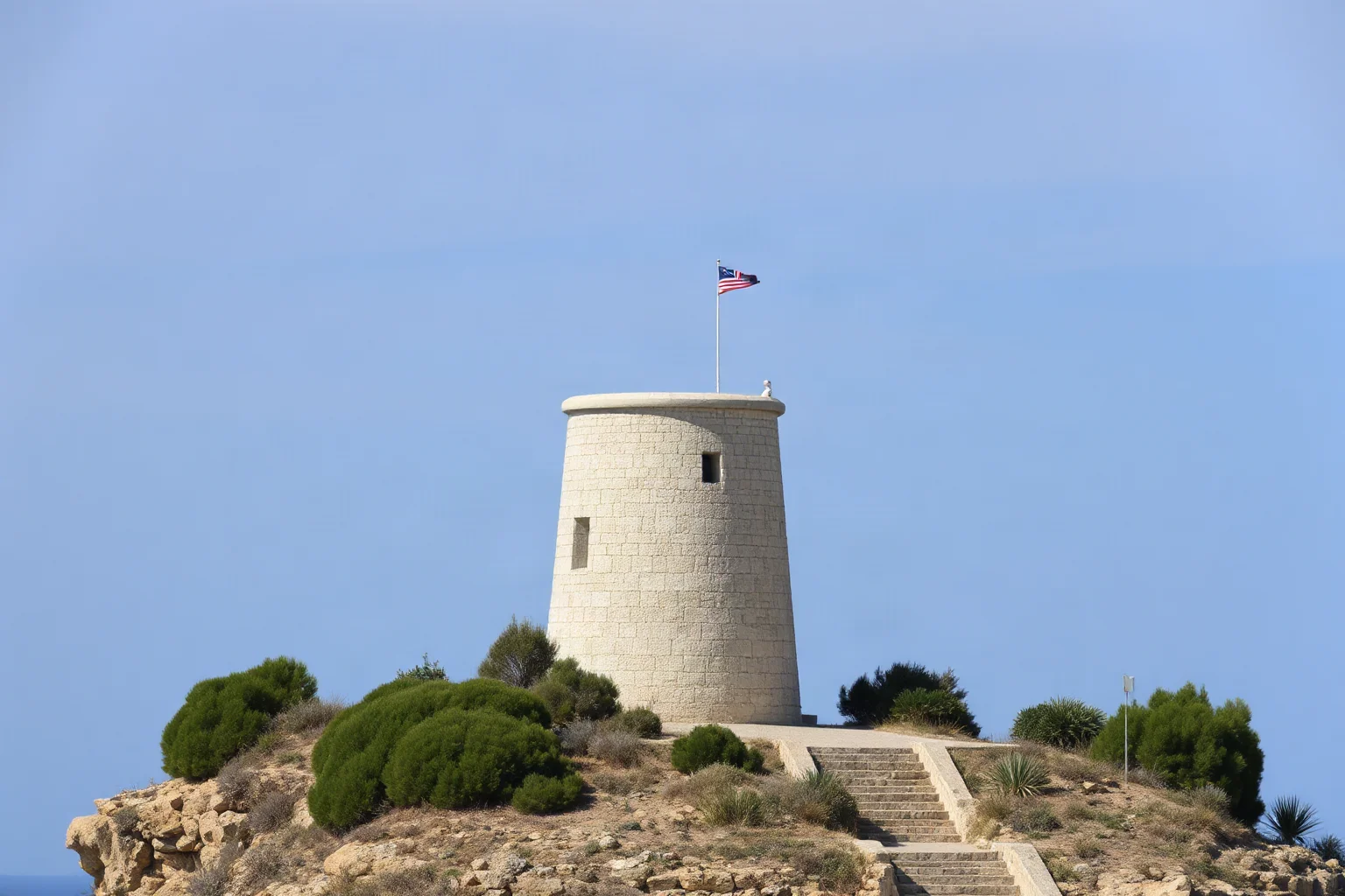 A conical dry-stone ancient tower structure standing alone in a Mediterranean island landscape