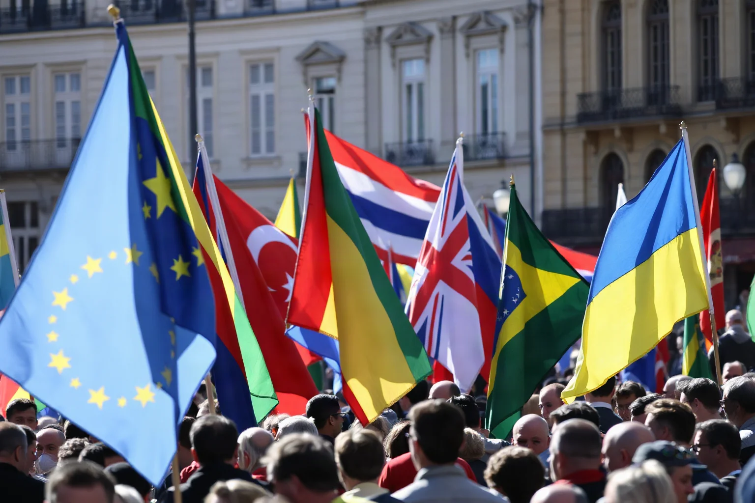 A crowd holding colorful flags and banners filling a European city square