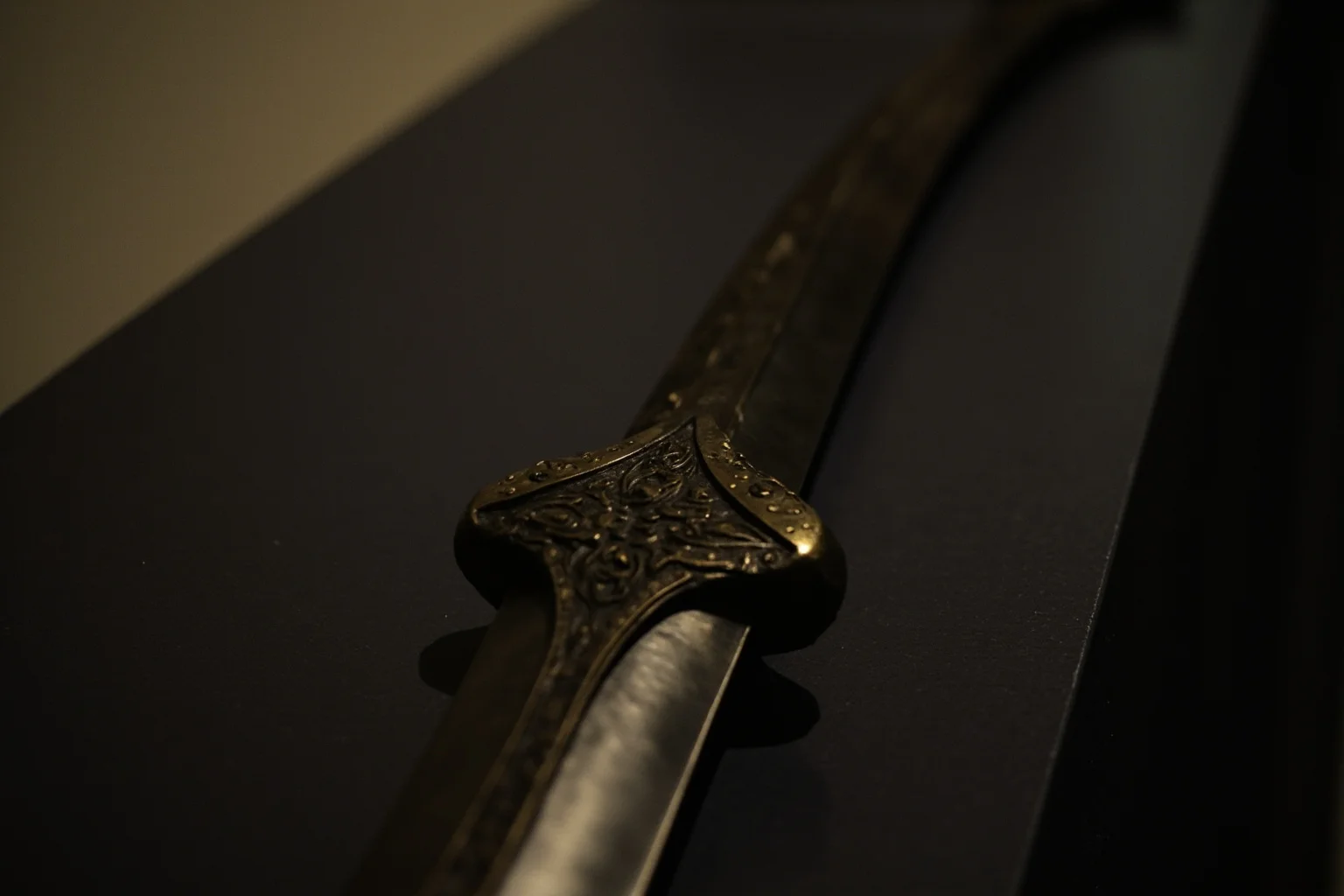 A curved medieval sword resting in a museum display case with dim protective lighting