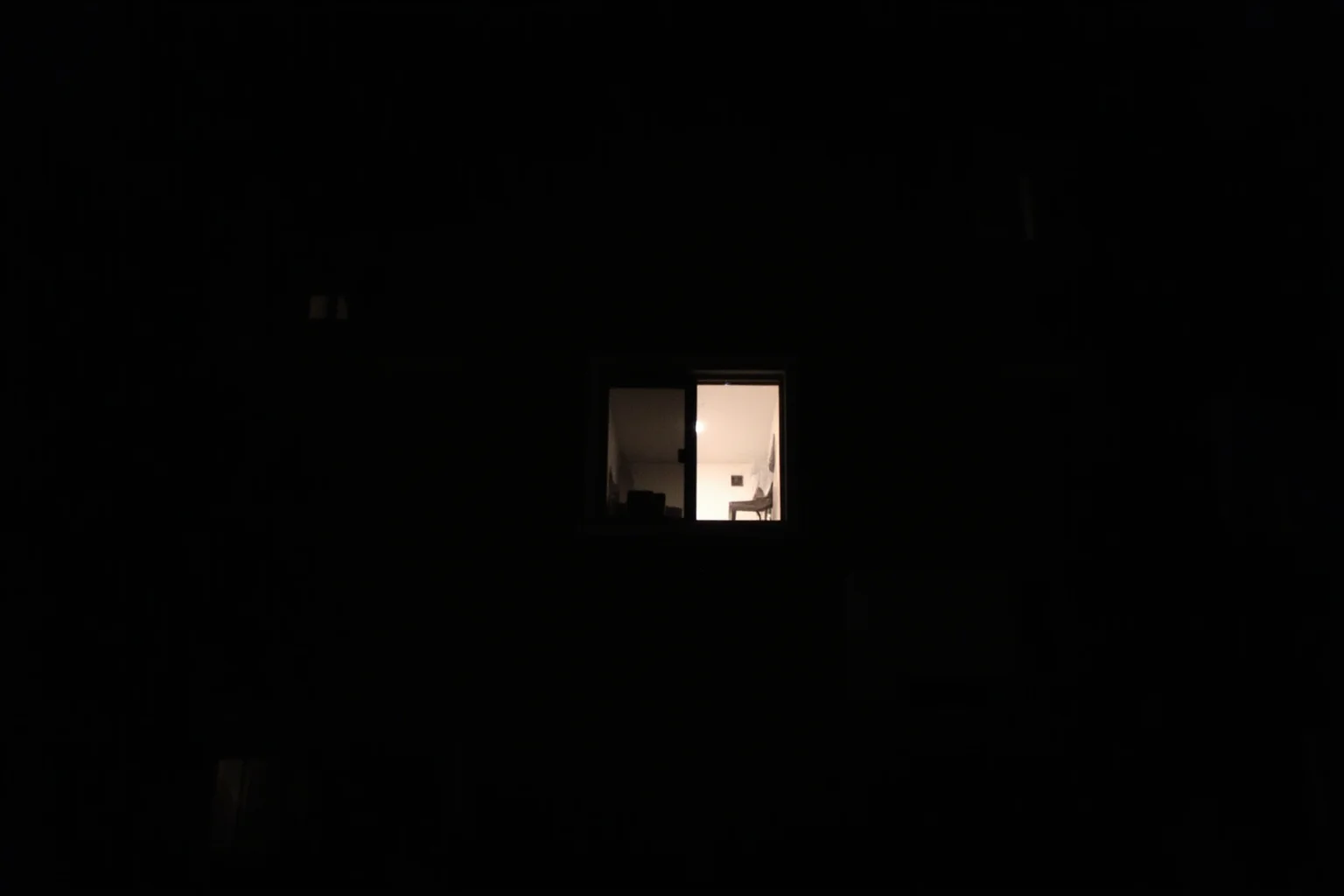 A dark suburban Milwaukee apartment building exterior at night with an eerie glow in one window