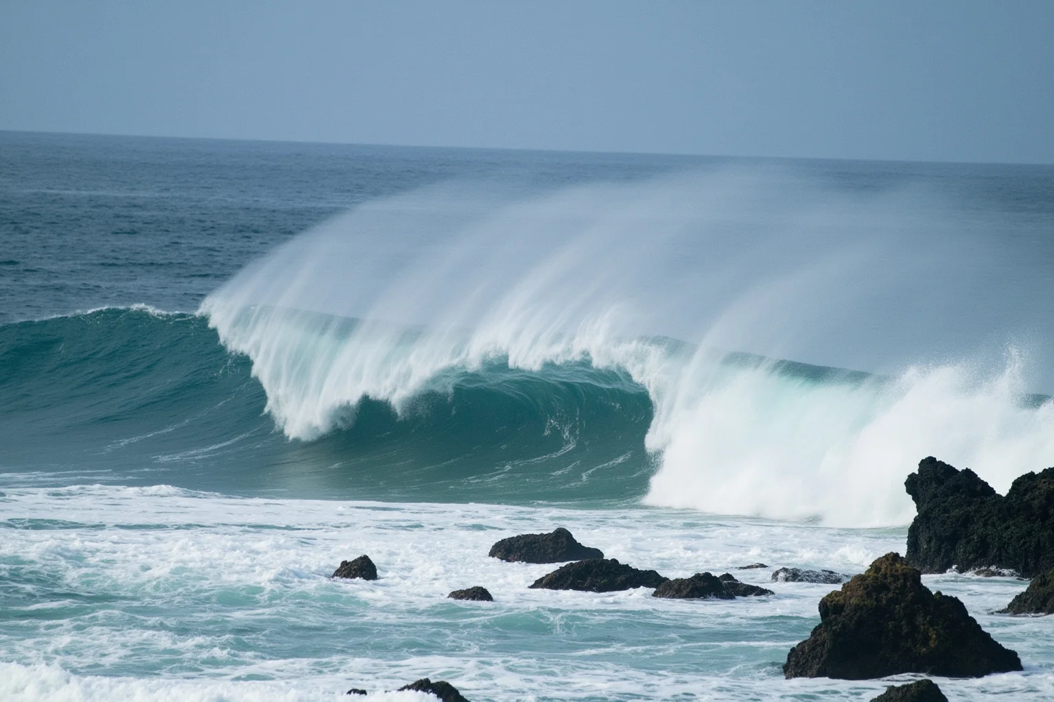A dramatic ocean rogue wave towering over small coastal rocks