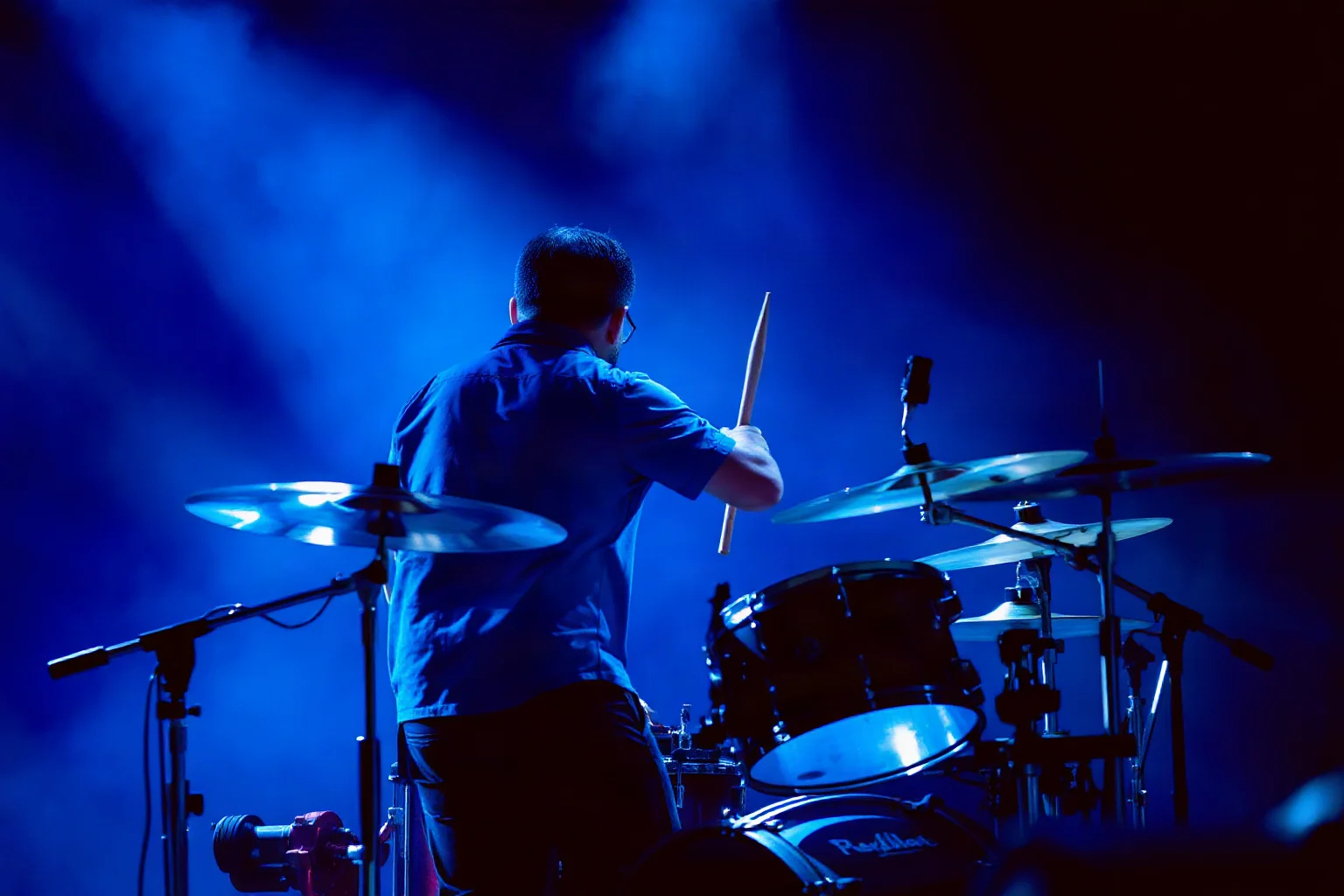 A drummer blending rock and jazz styles, intense concentration, moody blue stage lighting