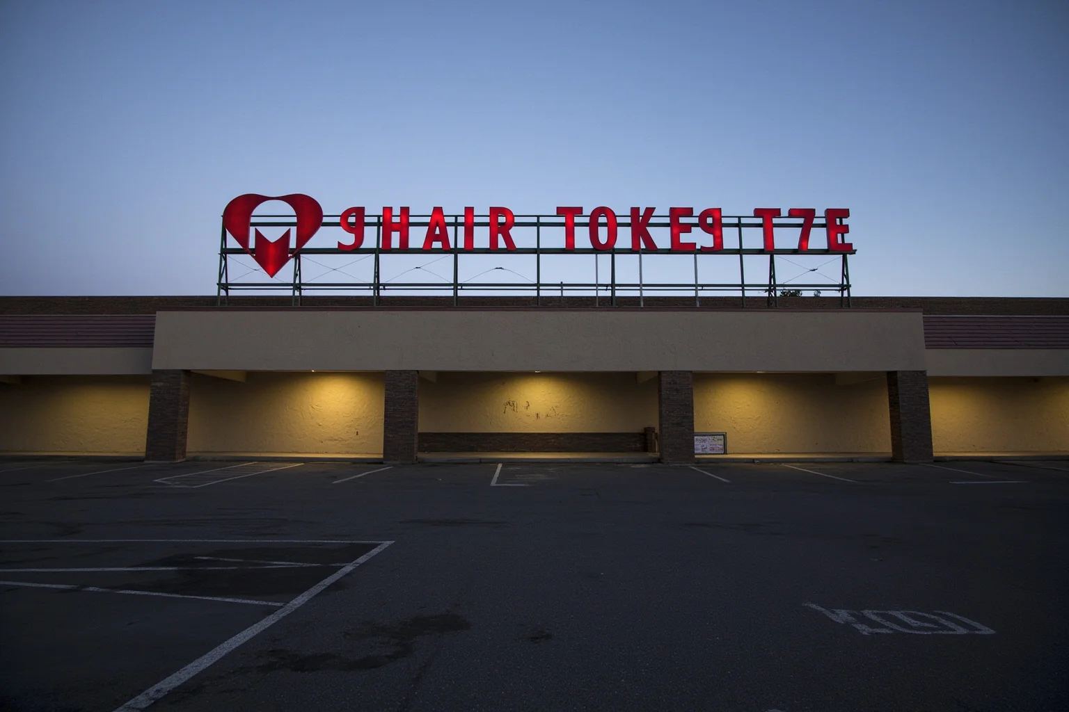 A faded department store sign above a mostly empty parking lot at dusk