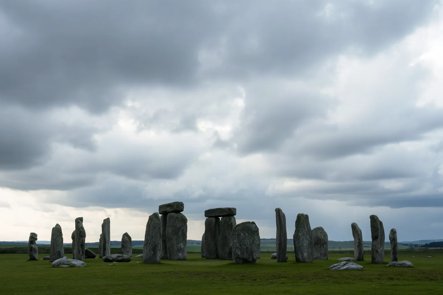A famous circle of massive standing stones on a green plain under a dramatic cloudy sky, no people