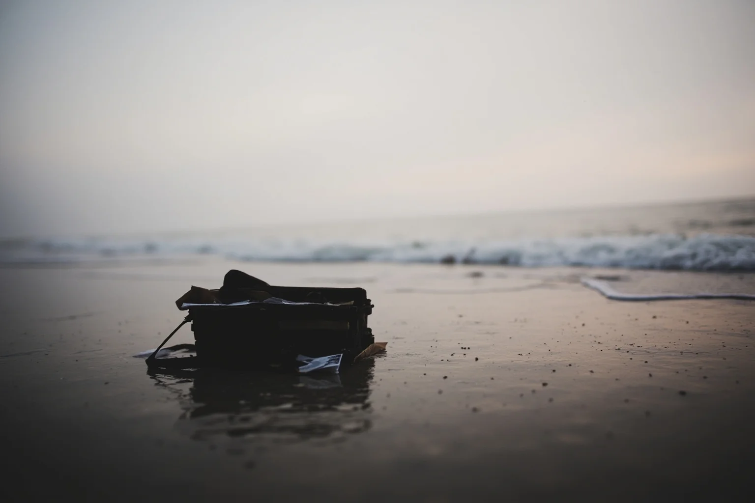 A foggy Spanish beach at dawn with a British military briefcase and papers washed ashore near the tideline