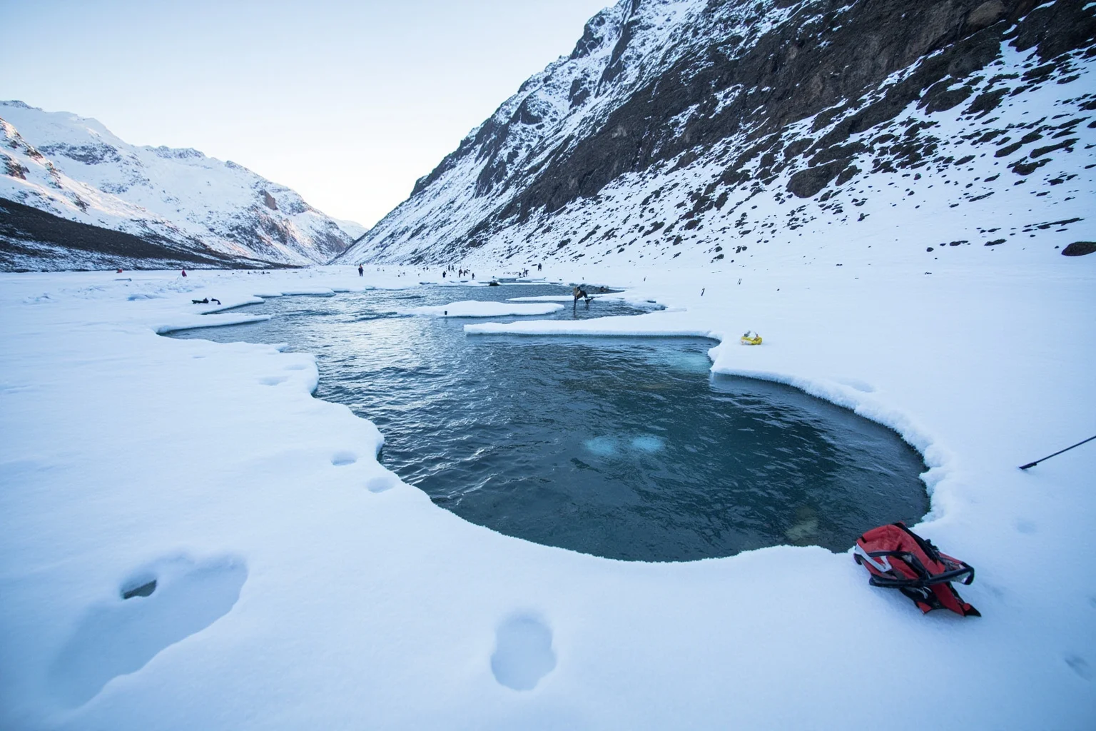 A frozen mountain stream with a broken hole in the ice and rescue gear scattered nearby