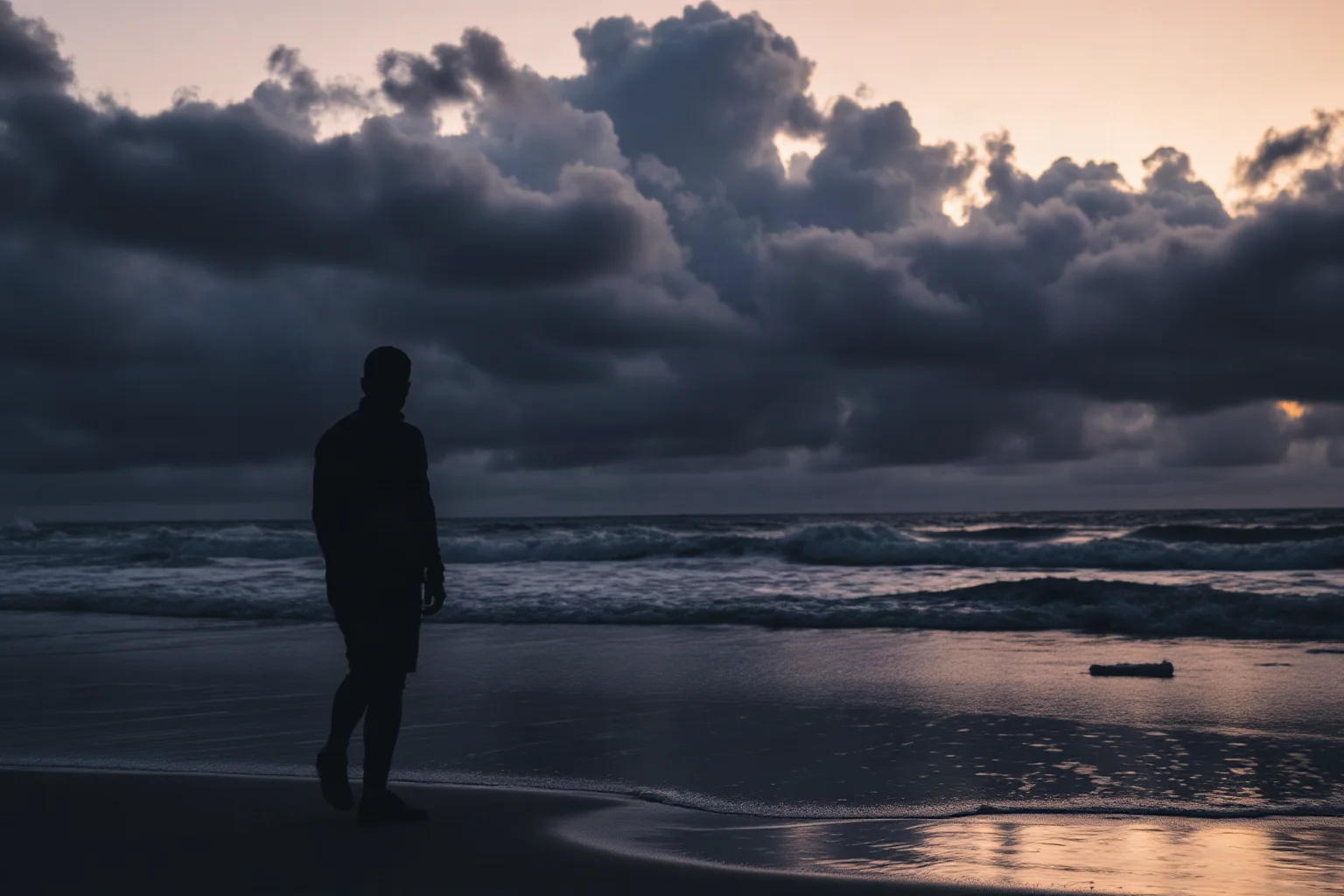 A ghostly gray silhouette of a man standing on a stormy beach at dusk with dark hurricane clouds gathering offshore