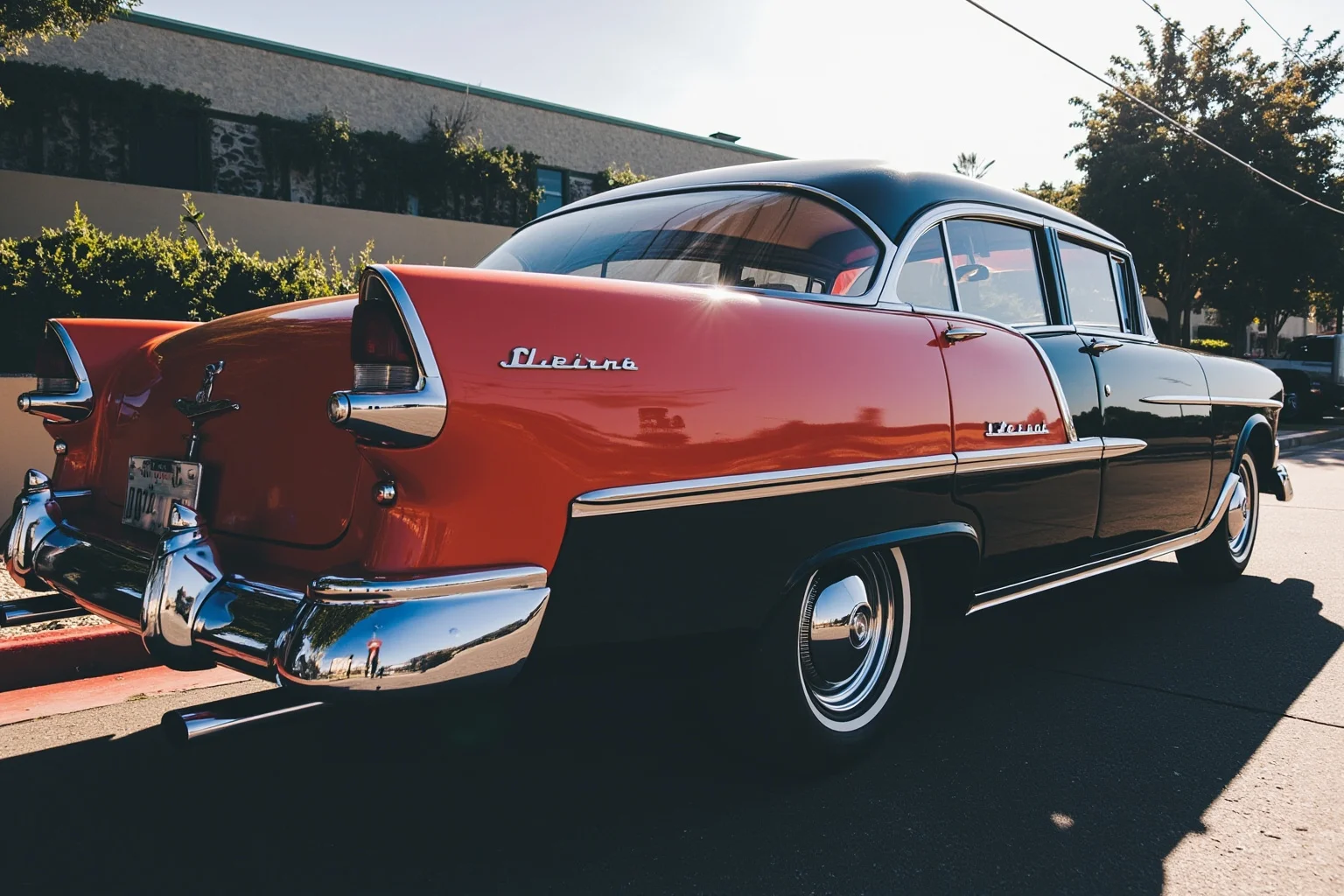 A gleaming 1950s two-tone sedan with tall tailfins and abundant chrome trim under bright sunlight