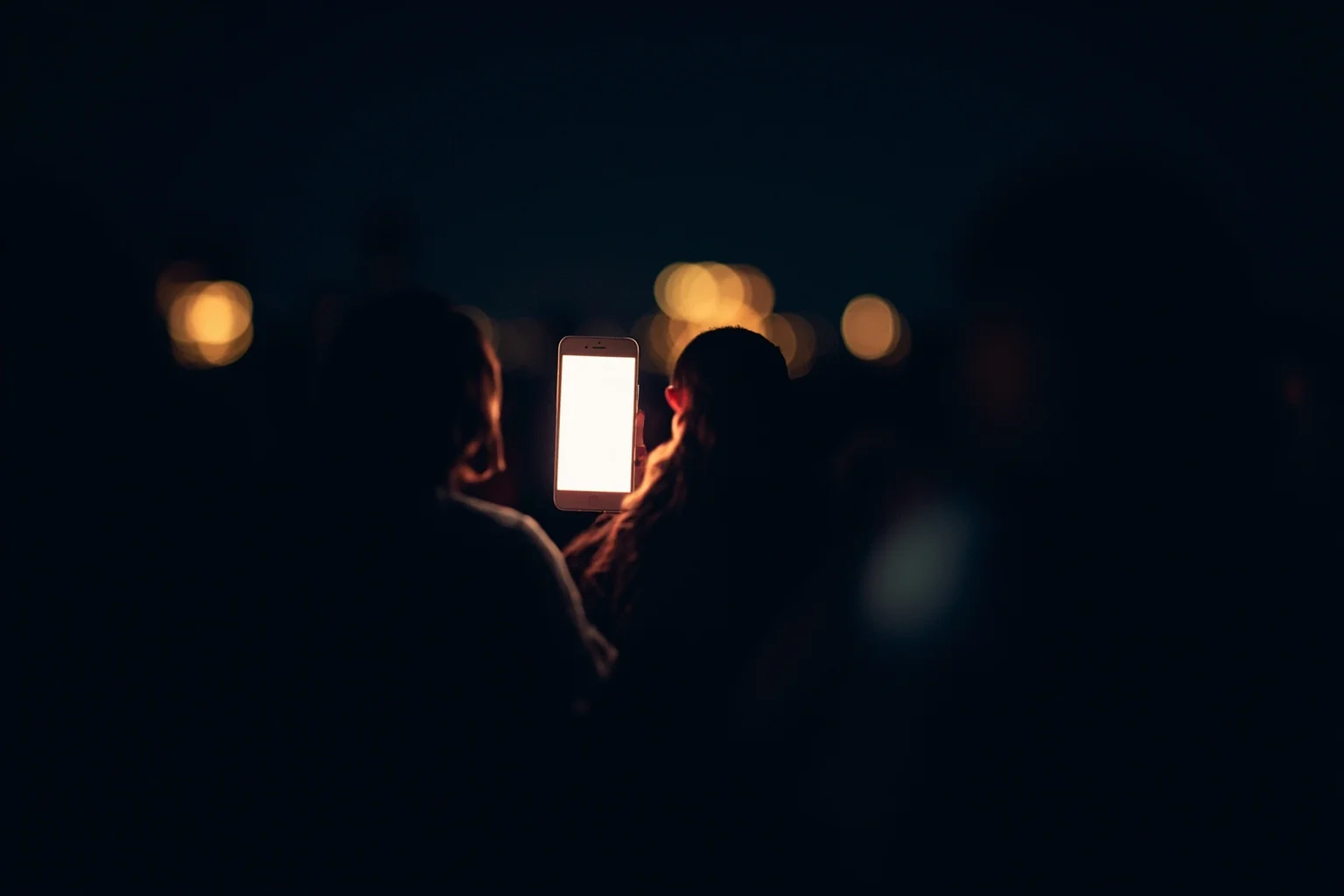 Brutal Forms of Public Humiliation Throughout History 22 A glowing smartphone screen surrounded by faint crowd silhouettes in the dark, symbolic modern illustration