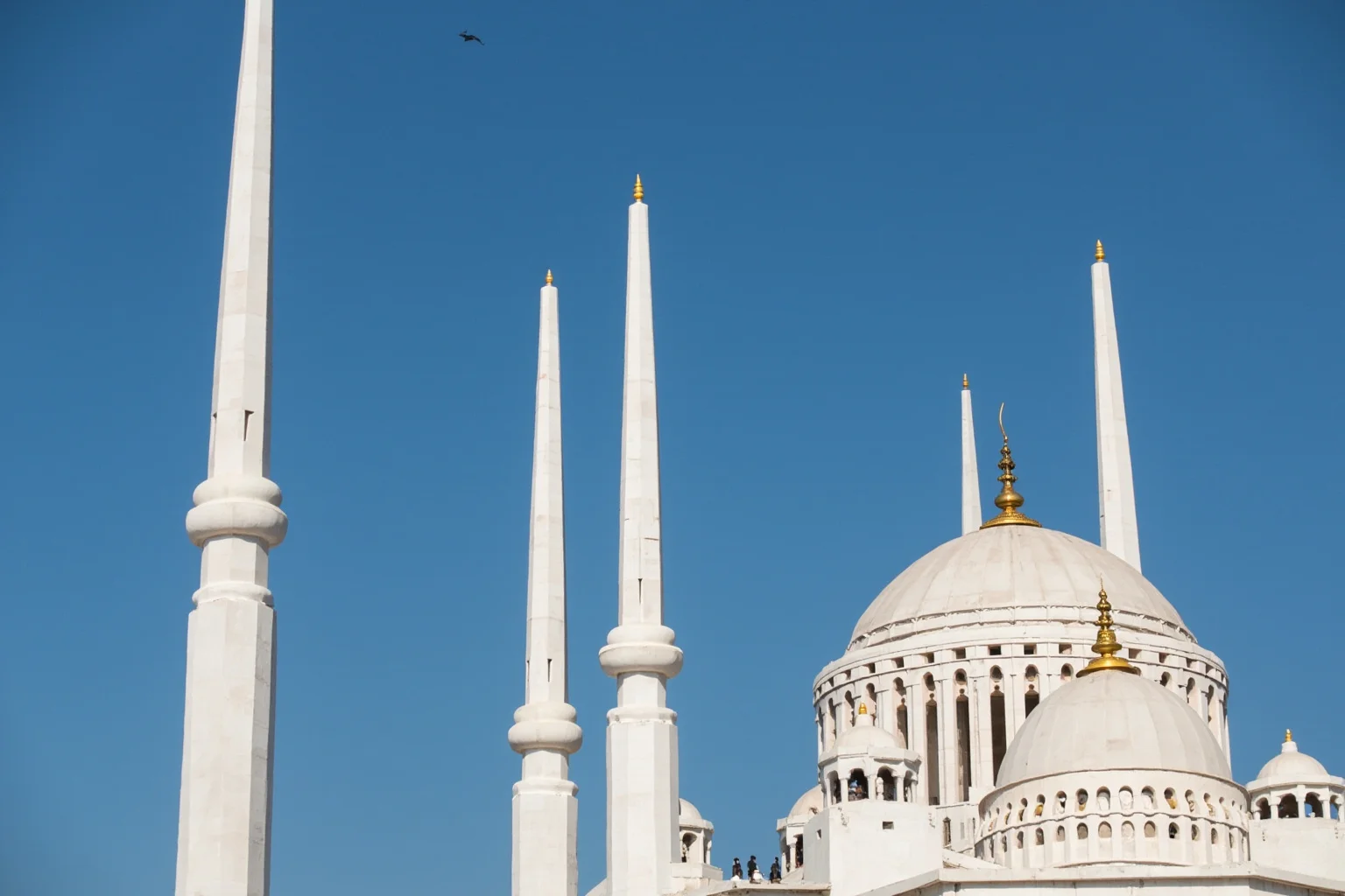 A grand domed marble mausoleum with four tall slender minarets leaning subtly outward against a blue sky