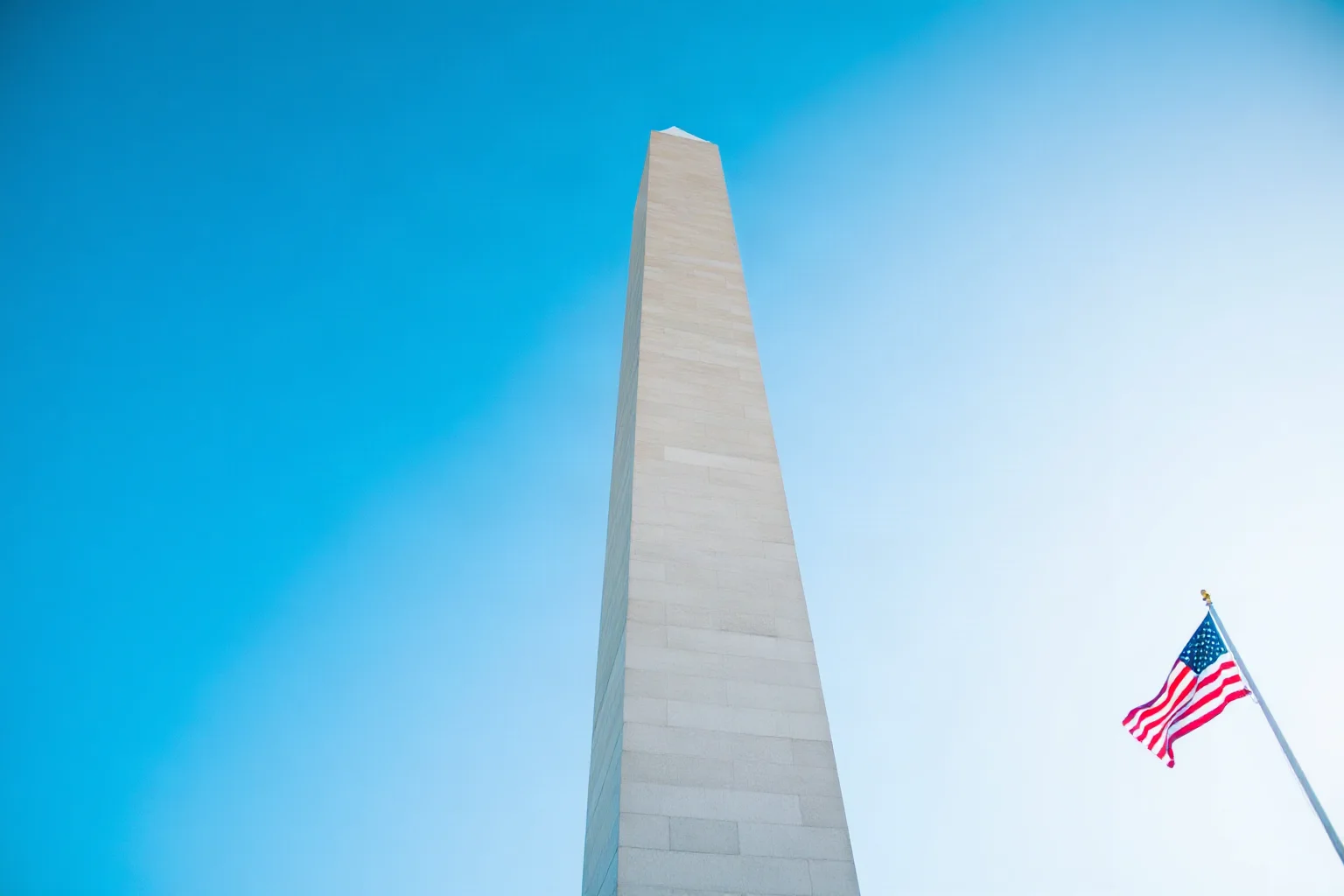 A grand stone monument obelisk against a blue sky with an American flag nearby, modern photograph style