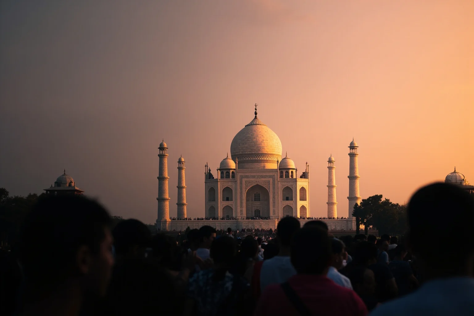 A grand white marble mausoleum glowing at sunset with a crowd of small silhouetted visitors admiring it from a distance