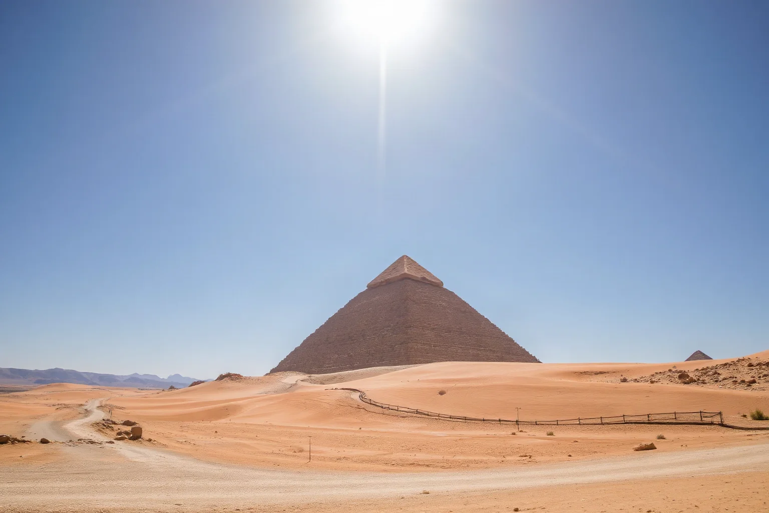 A great ancient stone pyramid rising from a desert landscape under bright daylight, wide angle