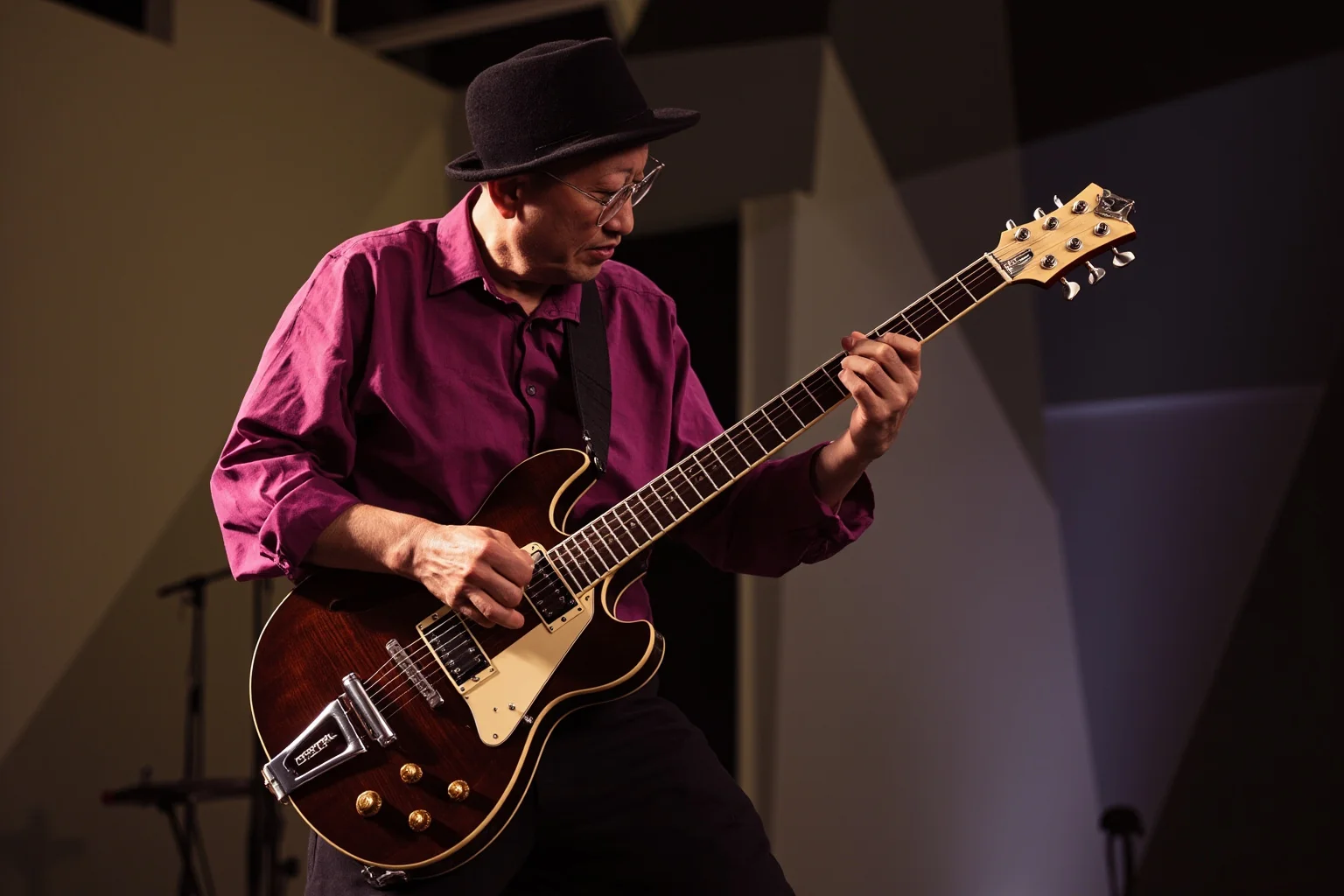 A jazz fusion guitarist playing a hollow-body electric guitar with complex rapid finger movement, abstract geometric stage backdrop
