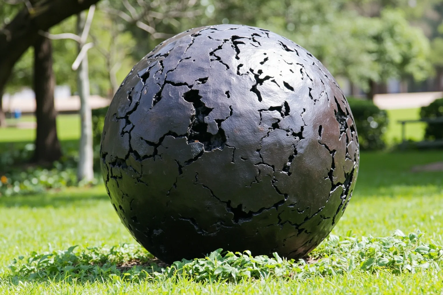 A large dented bronze globe sculpture displayed outdoors in a memorial park setting