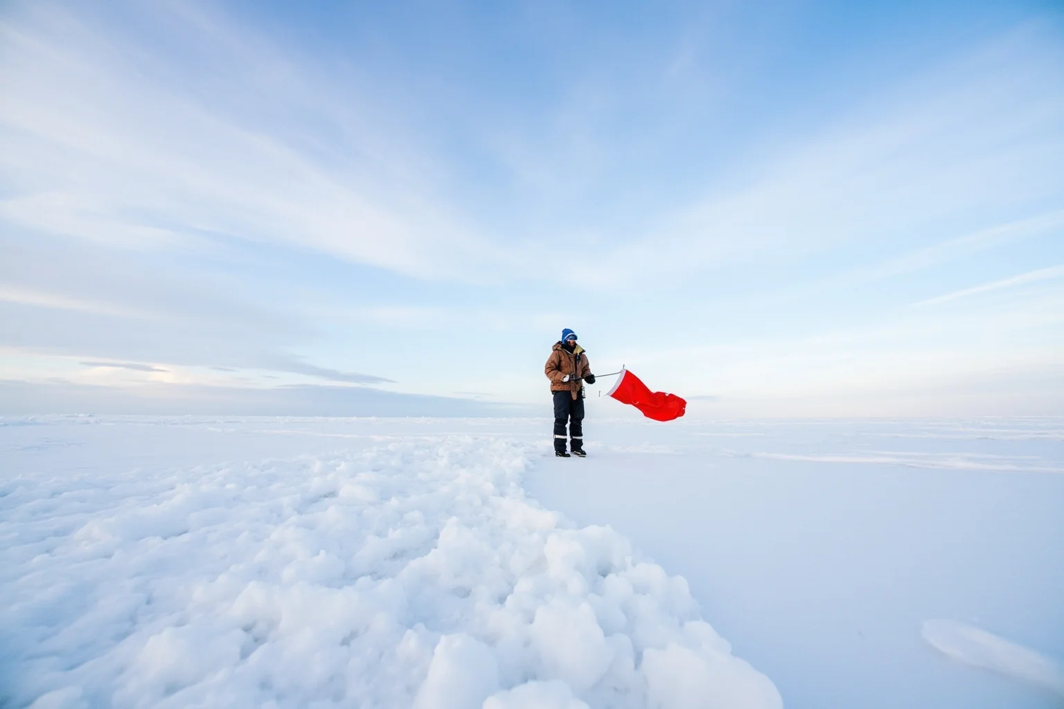 A lone explorer in Arctic furs planting a flag on a featureless expanse of sea ice near the horizon