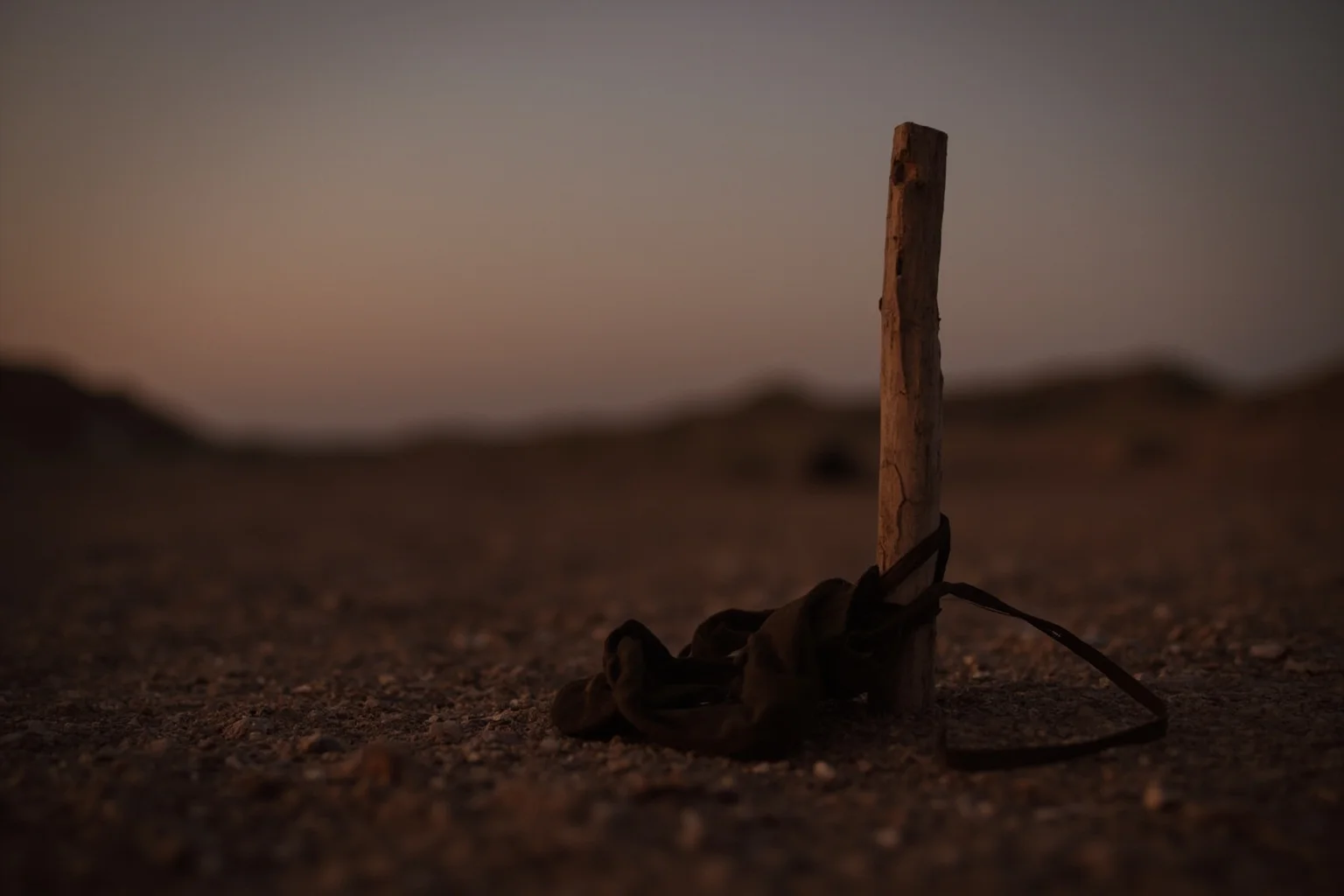 25 Disturbing Last Words By Notorious Criminals 5 A lone wooden stake and blindfold on the ground at dawn, symbolizing a firing squad execution, desert landscape, somber tone