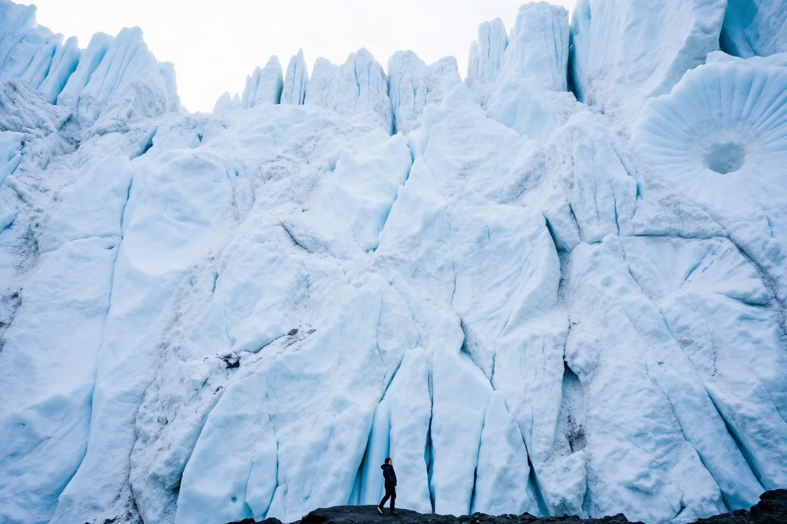 A massive wall of glacial ice towering over a small human figure for scale
