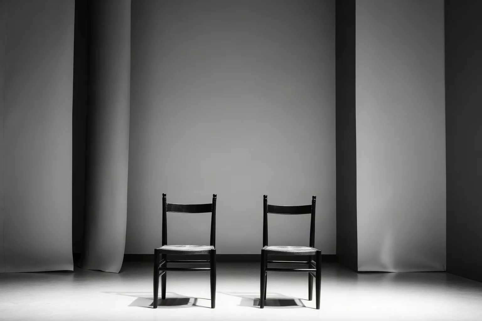 A minimalist black-and-white stage set with two bare chairs, evoking absurdist theater