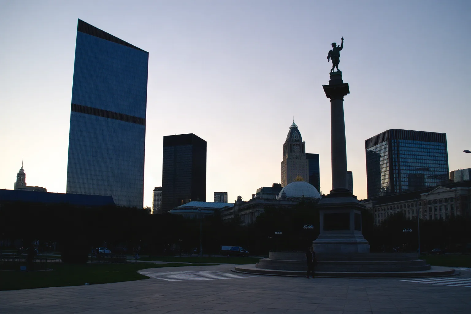 A modern city skyline at dusk with a historic monument in the foreground, illustrating a city's lasting memory and legacy