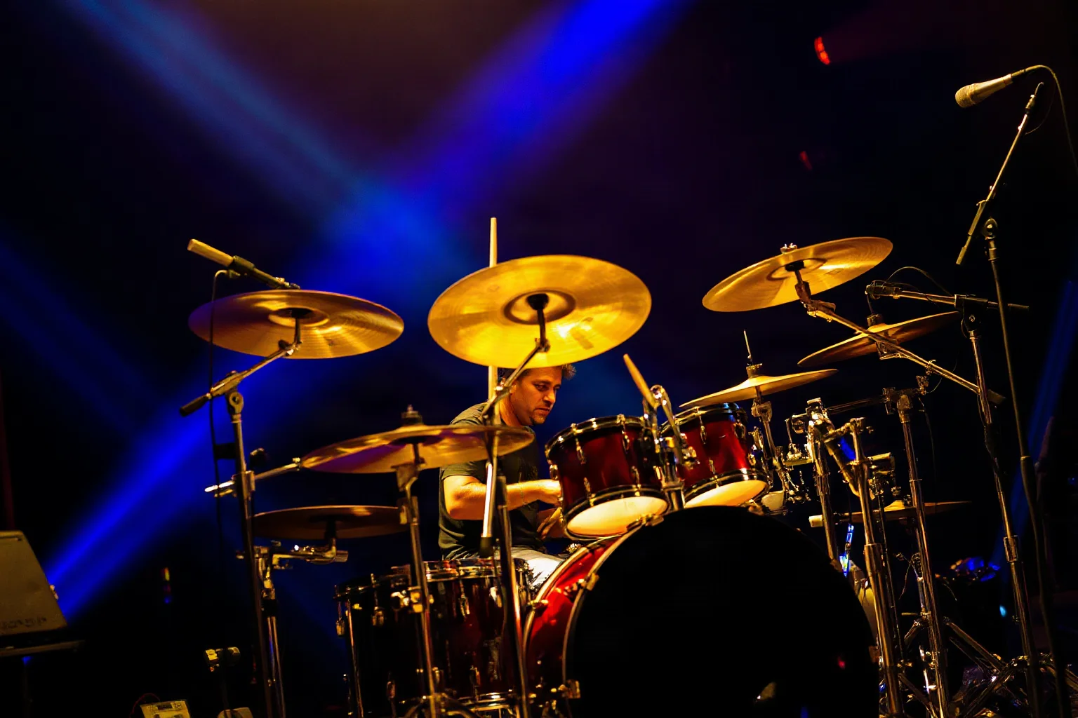 A modern progressive metal drummer playing an elaborate kit with world percussion elements under blue stage light