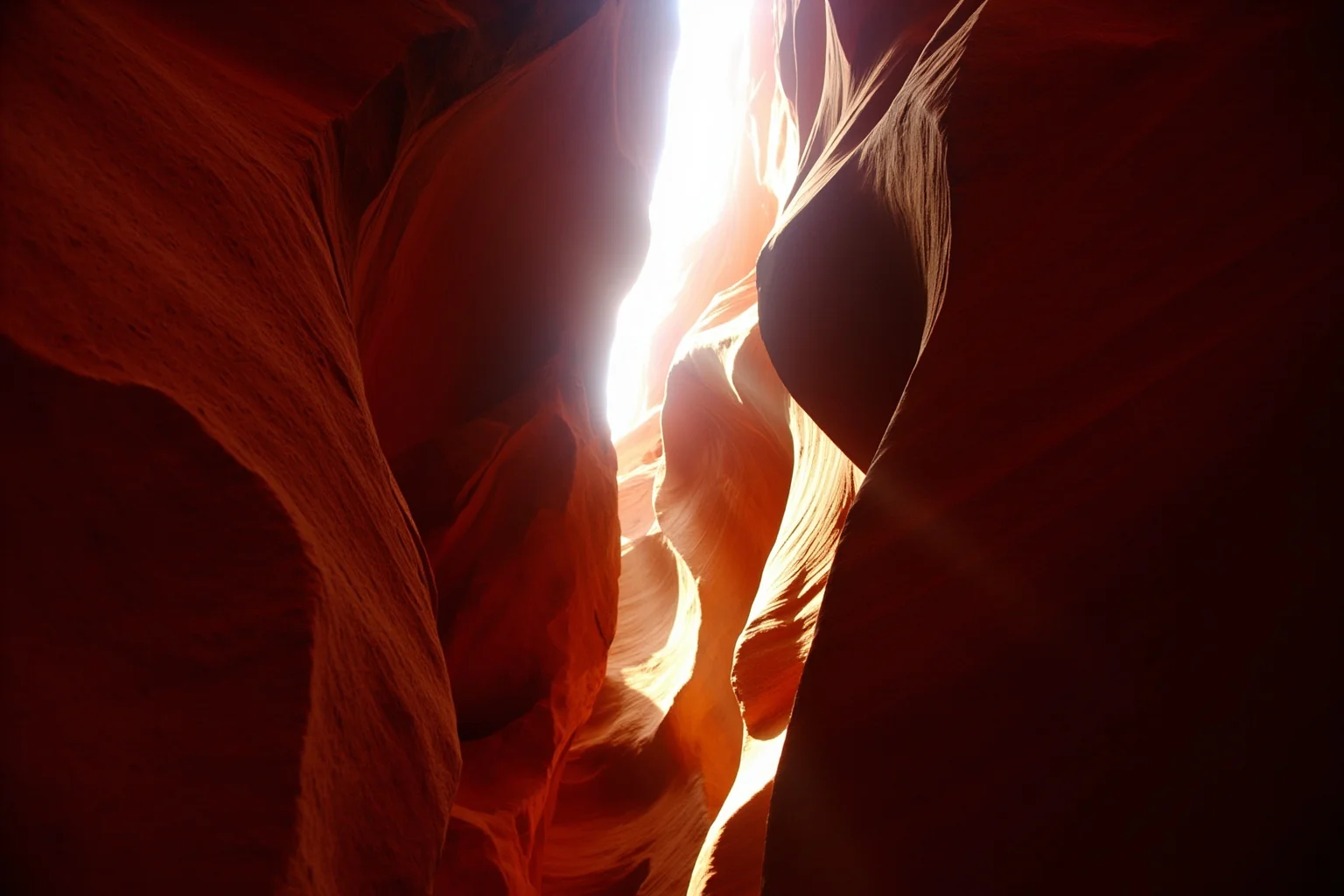 A narrow slot canyon with sunlight streaming down between red sandstone walls