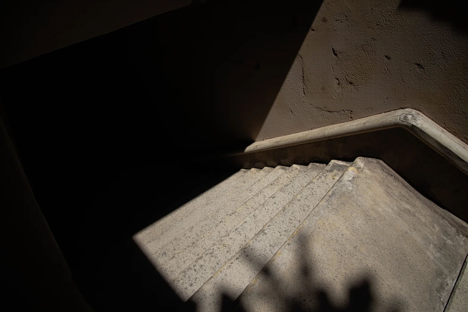 A narrow stone staircase in an old European building with two shadows passing