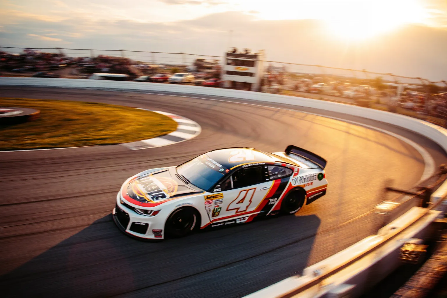 A NASCAR stock car racing around a high-banked oval track at Daytona, dramatic speed blur, golden hour lighting