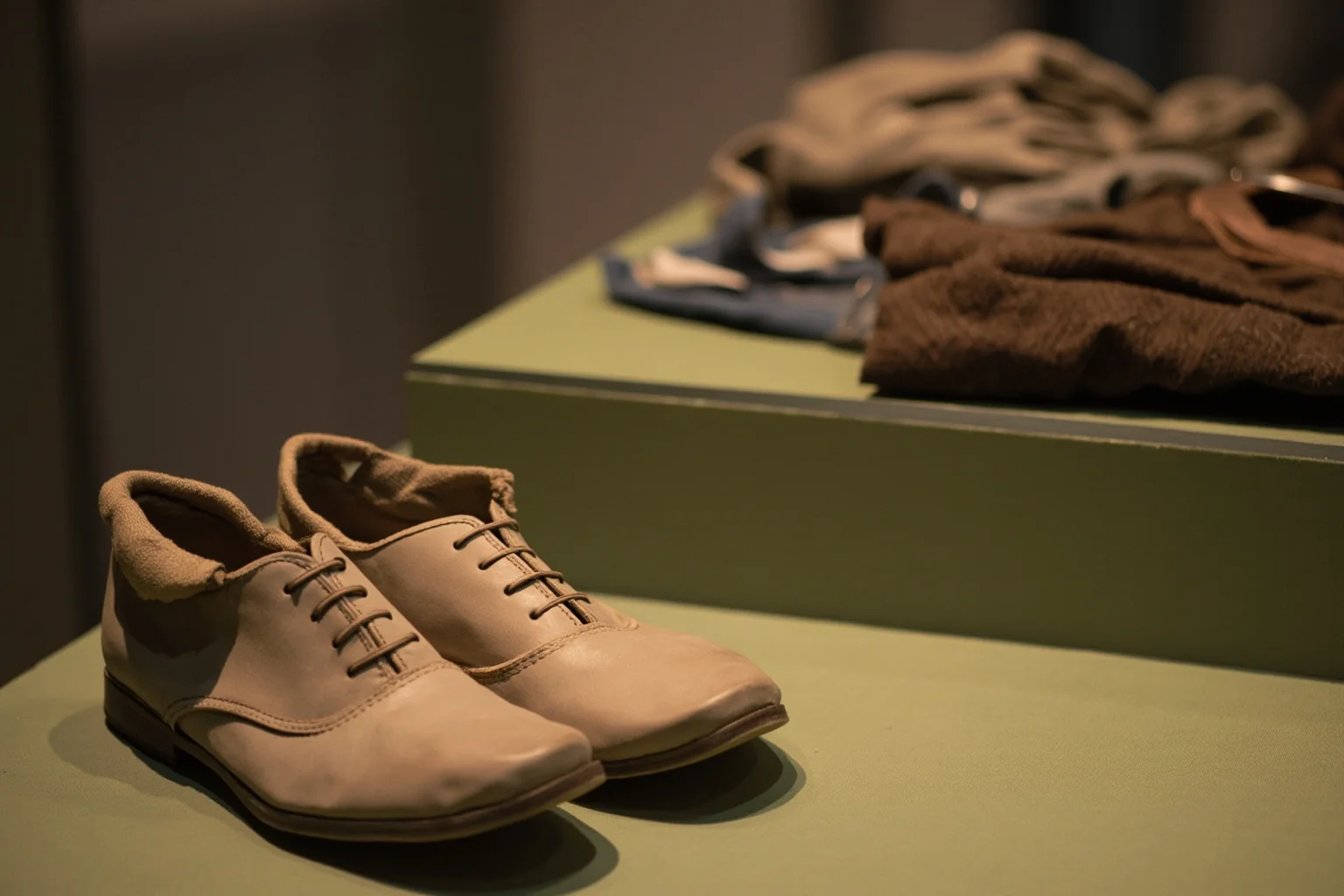 A pair of dust-covered shoes and folded clothing displayed in a museum glass case