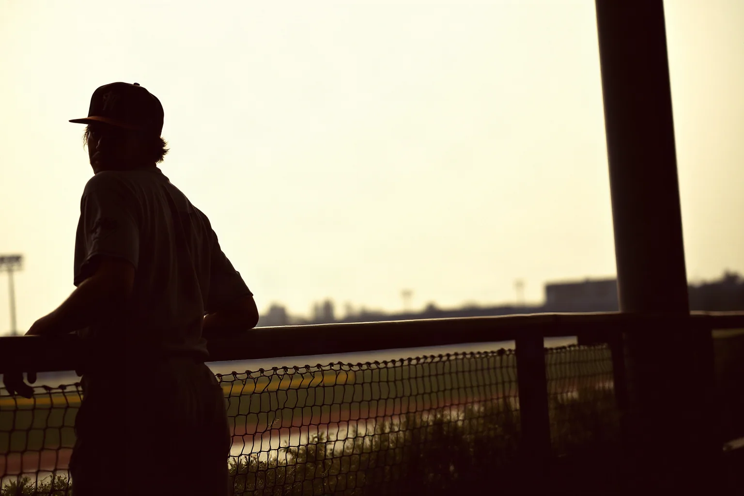 A pitcher's silhouette looking tired and worn, leaning on a dugout rail, faded vintage color palette
