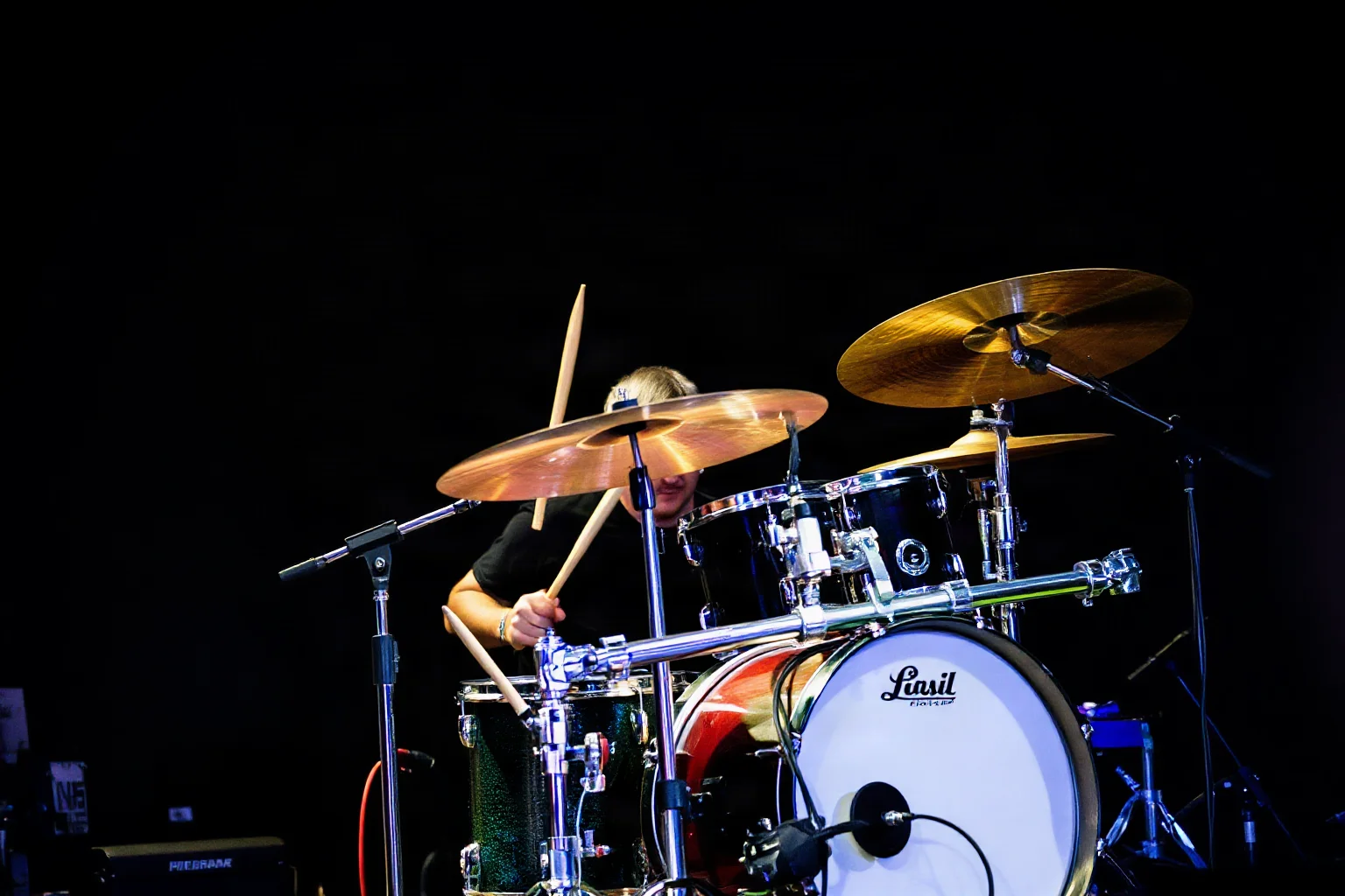A progressive rock drummer playing an asymmetrical, unconventional drum kit in dim stage lighting