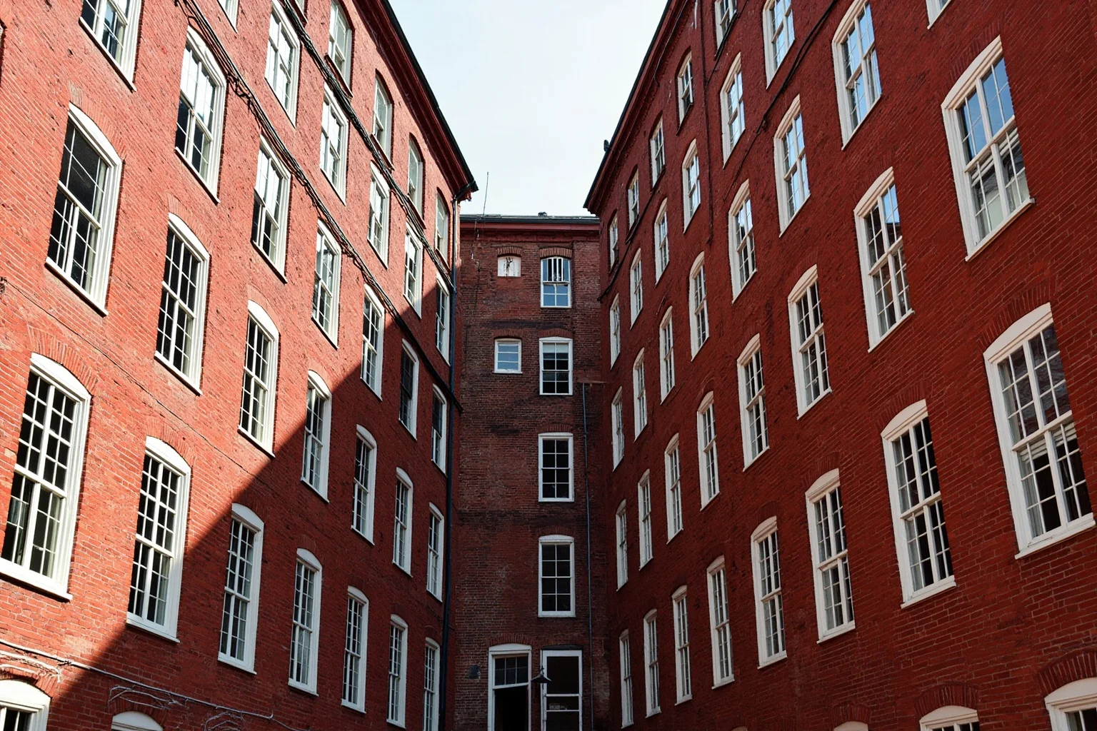 A red-brick New England textile mill complex with rows of windows, early 1800s style