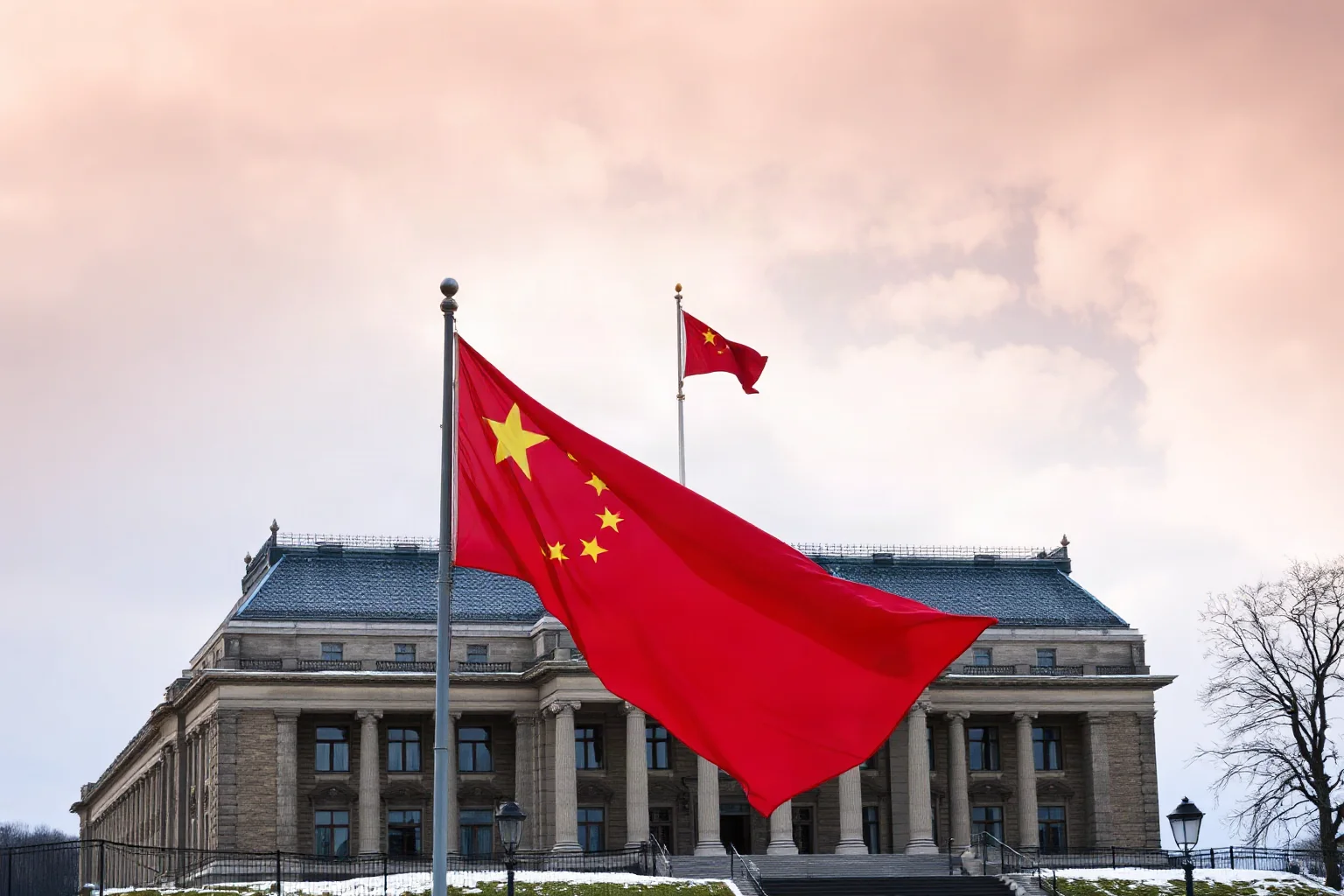 A red flag waving over a grand government building under a wintry sky
