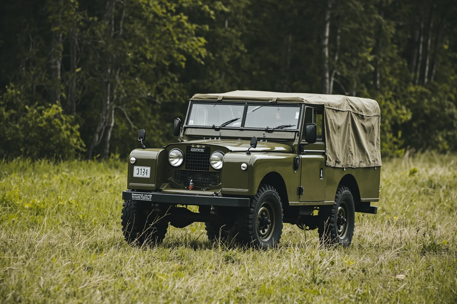 A rugged olive-green military utility vehicle with a flat hood and canvas top driving through a wooded field