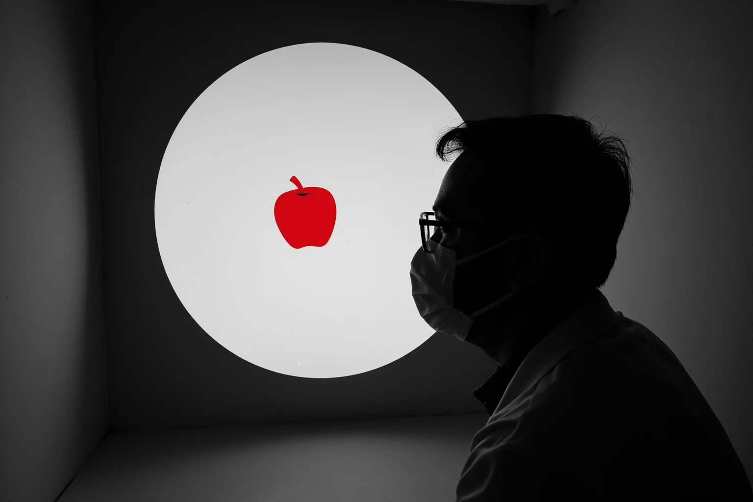 A scientist in a black-and-white room looking through a window at a single vivid red apple